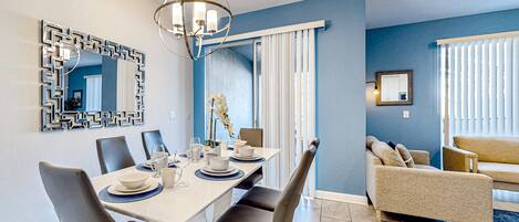 A dining area with a table set for four, chairs, a chandelier, and a large mirror on the wall.