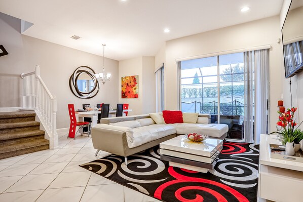 A modern living room with a sectional sofa, a dining area, and a staircase. - Family-friendly Home With Private Pool, Wifi, Central AC, & Private Washer/dryer (Davenport)
