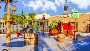 A water feature with wooden barrels, a palm tree, and a building with a white fence in the background. - Family-friendly Home With Private Pool, Wifi, Central AC, & Private Washer/dryer (Davenport)