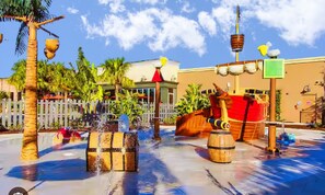 A water feature with wooden barrels, a palm tree, and a building with a white fence in the background. - Family-friendly Home With Private Pool, Wifi, Central AC, & Private Washer/dryer (Davenport)