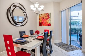 A dining area with a white table, black and red chairs, a chandelier, a large mirror, and a painting of flowers. - Family-friendly Home With Private Pool, Wifi, Central AC, & Private Washer/dryer (Davenport)