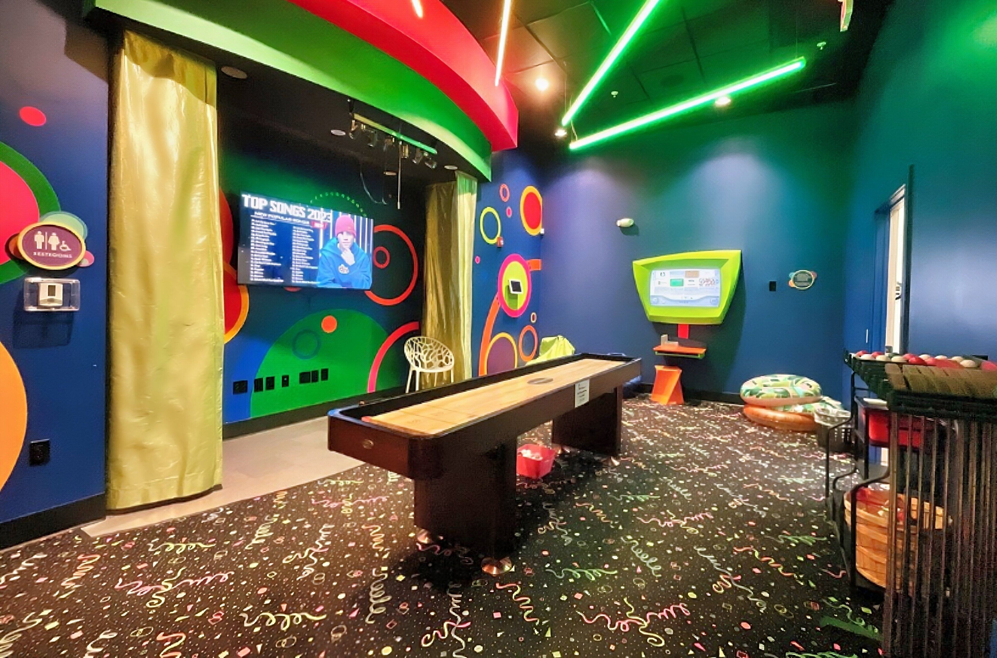 Una mesa de billar, una pantalla de televisión y una pared con diseños circulares de colores.