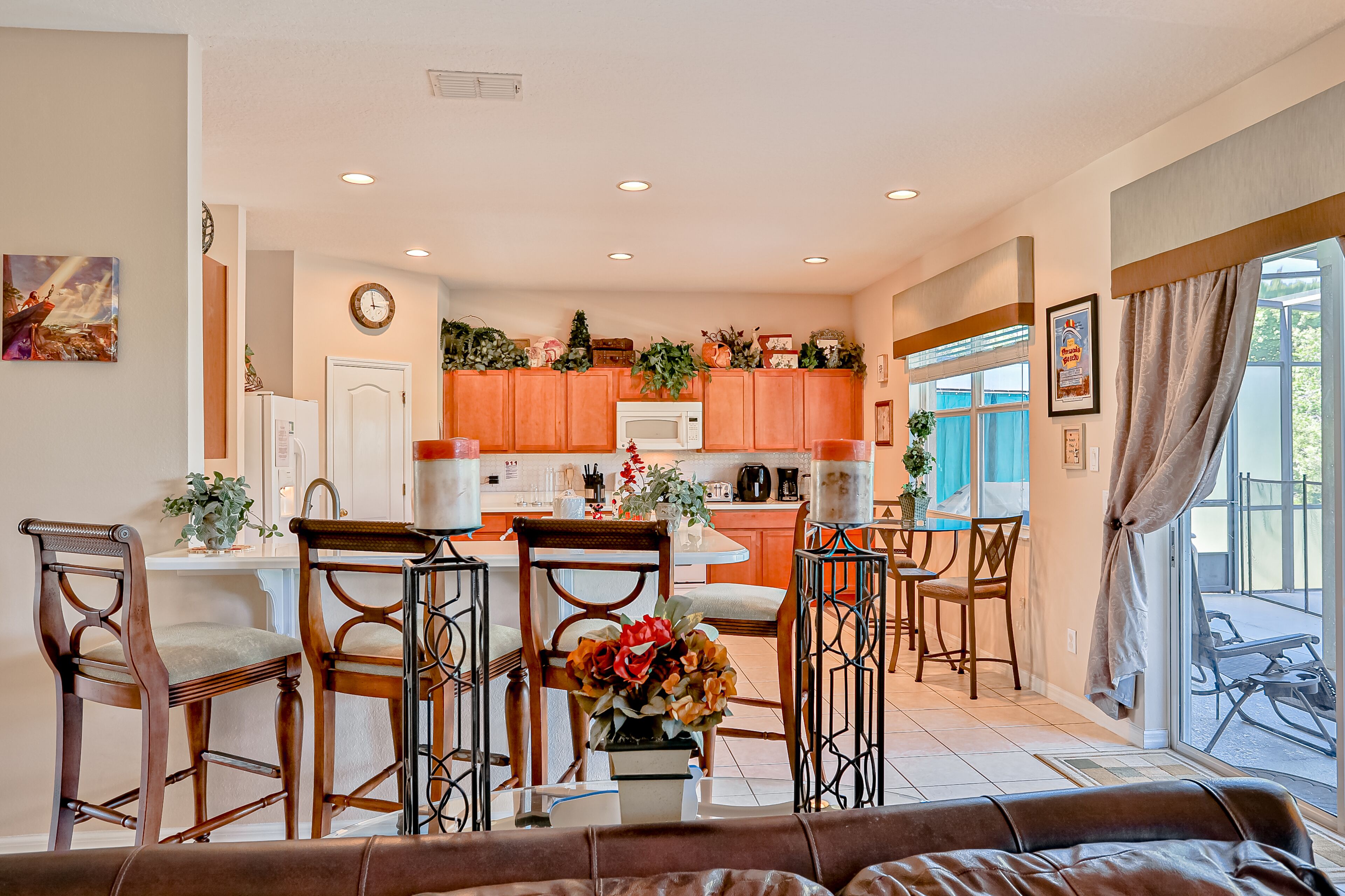 A spacious living area with a sofa, a dining table with chairs, a kitchen with orange cabinets, and a large window with curtains.