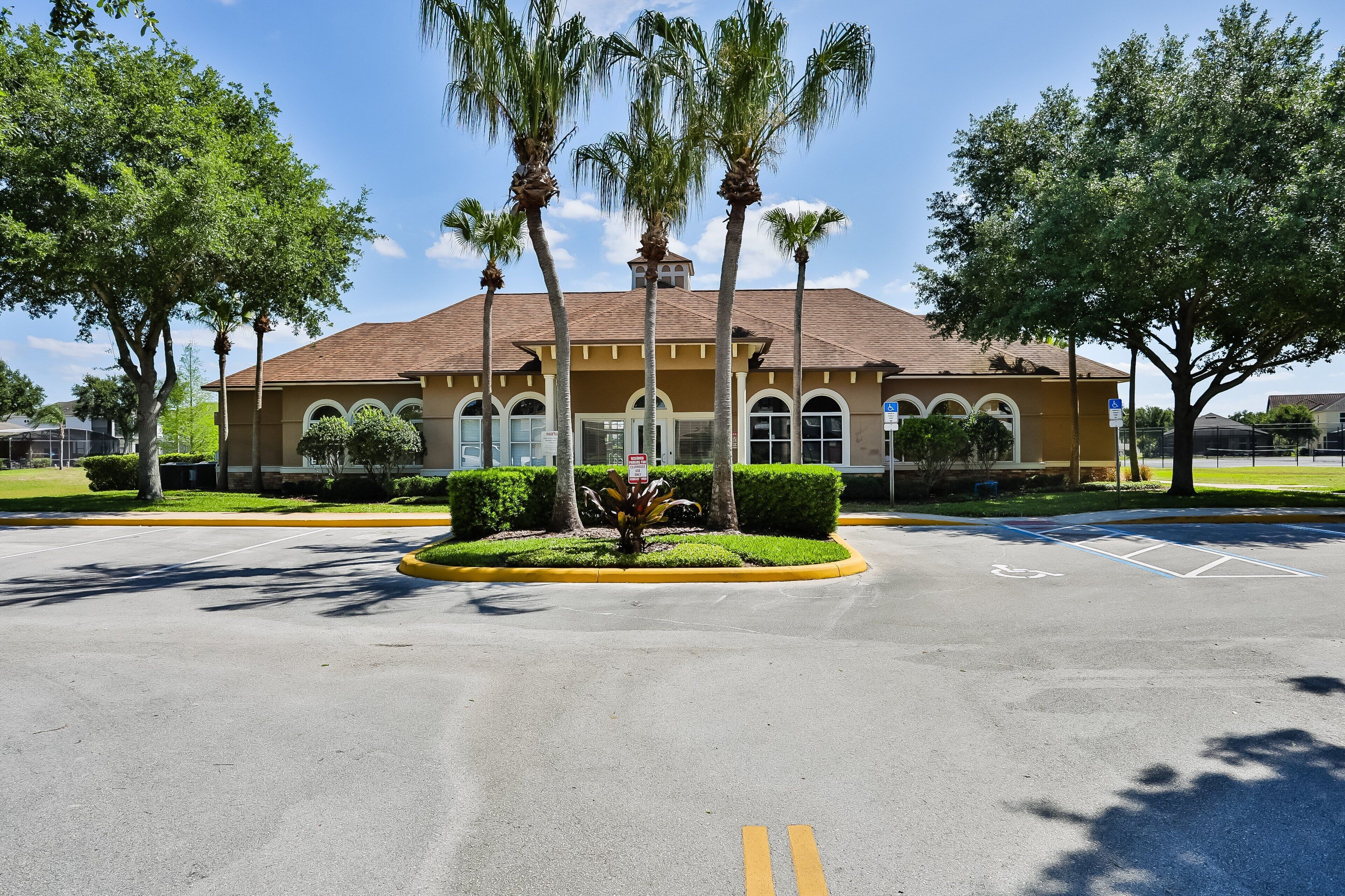 A building with a brown roof, palm trees, and a parking lot.