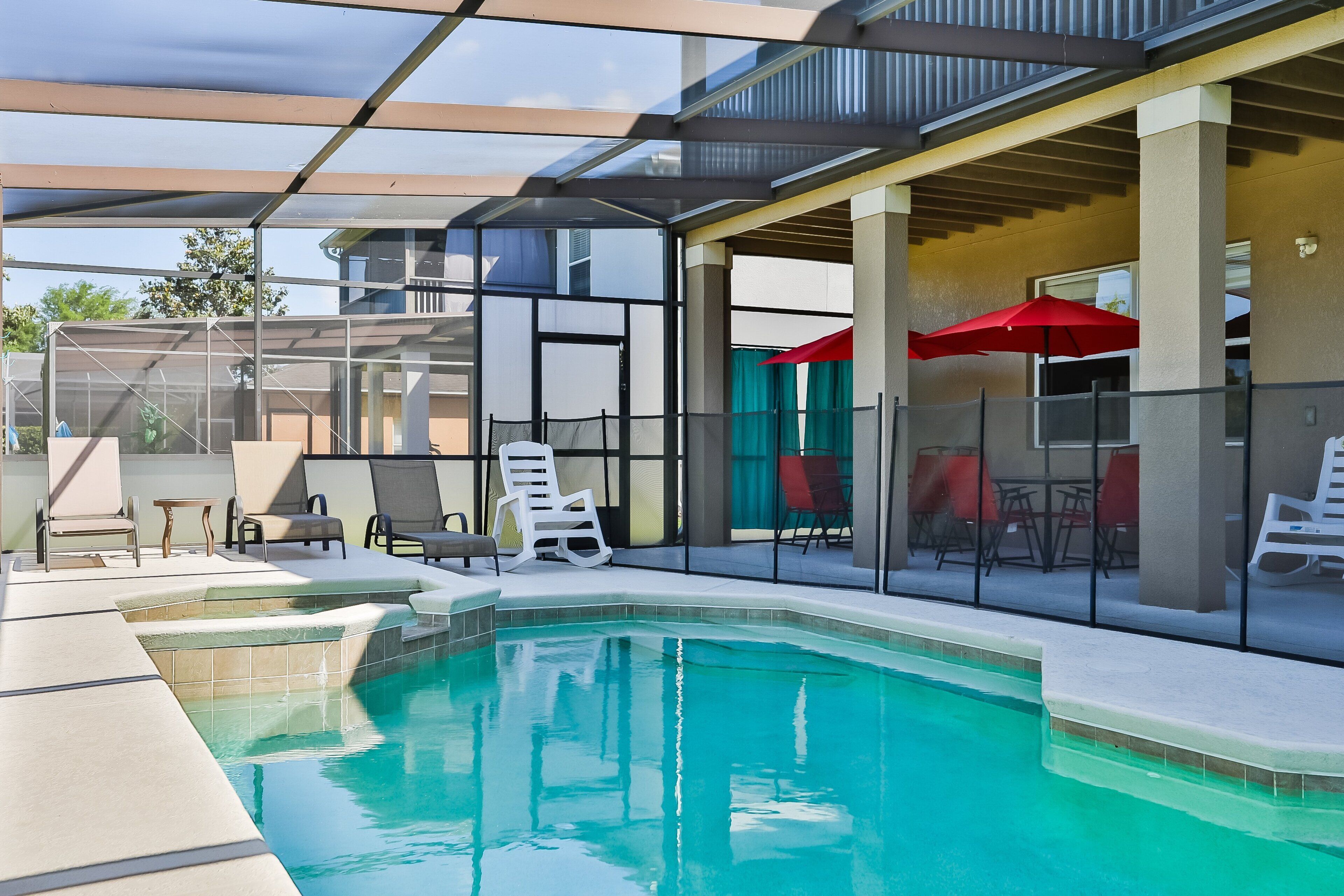 A modern indoor pool with clear glass walls, lounge chairs, and red umbrellas.