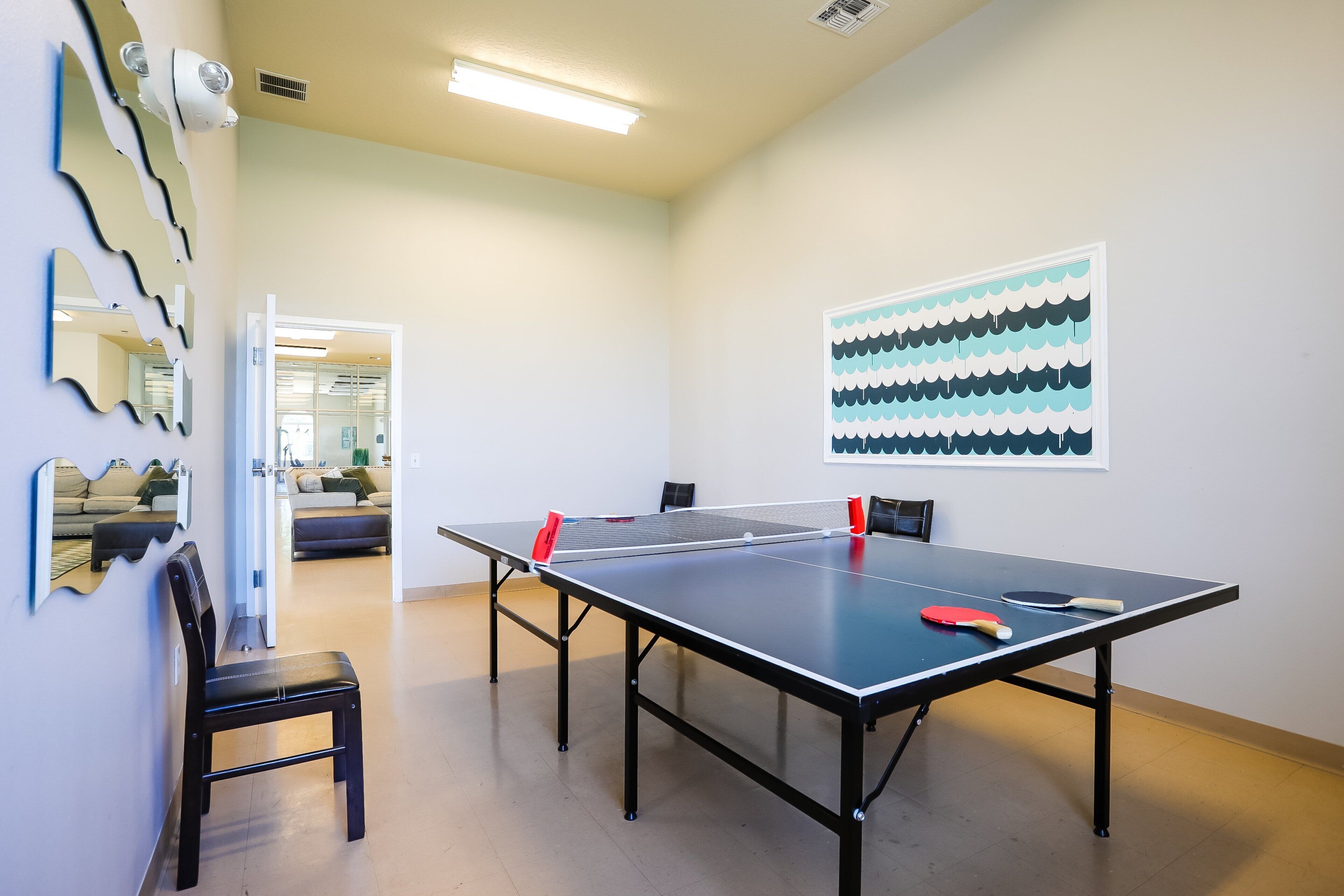 Una mesa de ping pong en una habitación con una silla, un espejo en la pared y una puerta que da a otra sala.