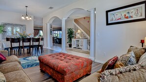 A spacious living room with a red ottoman, a dining area with a table and chairs, and a staircase leading to another level. - Stunning House With Lanai, Pool, Ping-pong, Full Kitchen, & Wifi (Davenport)