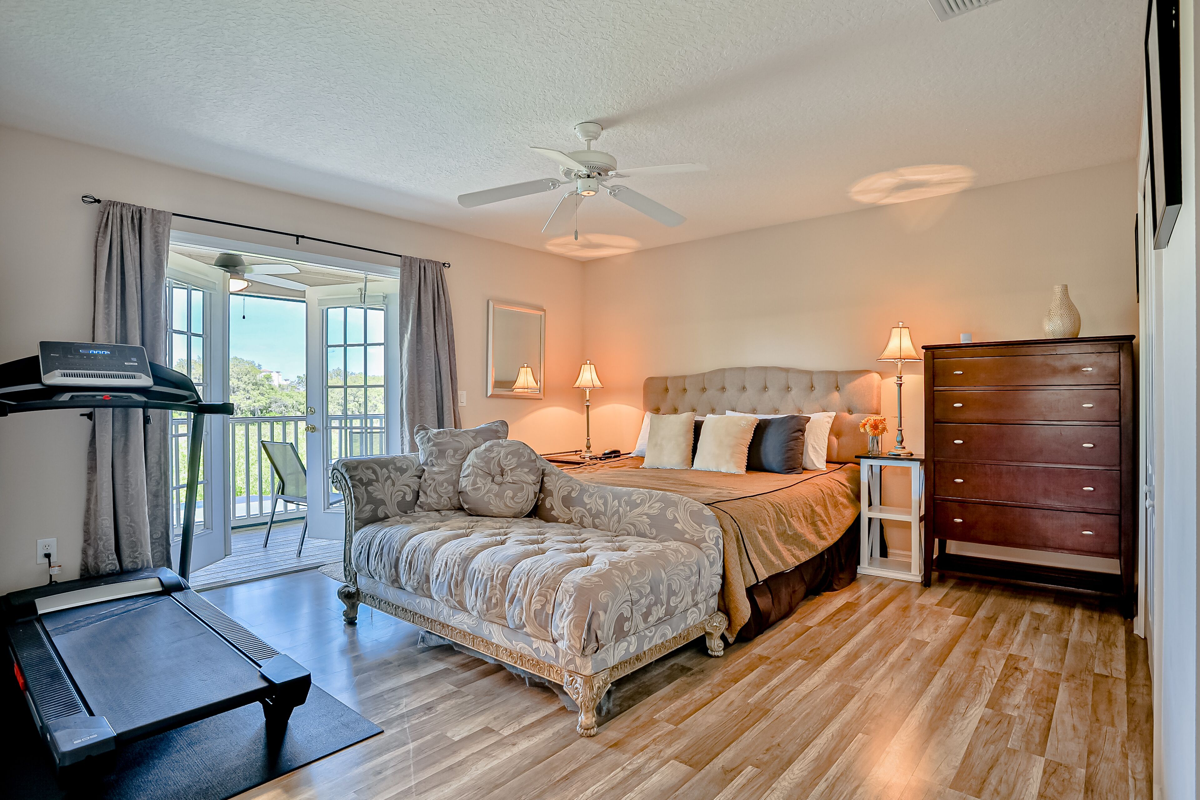A bedroom with a large bed, a treadmill, and a view of the outdoors.
