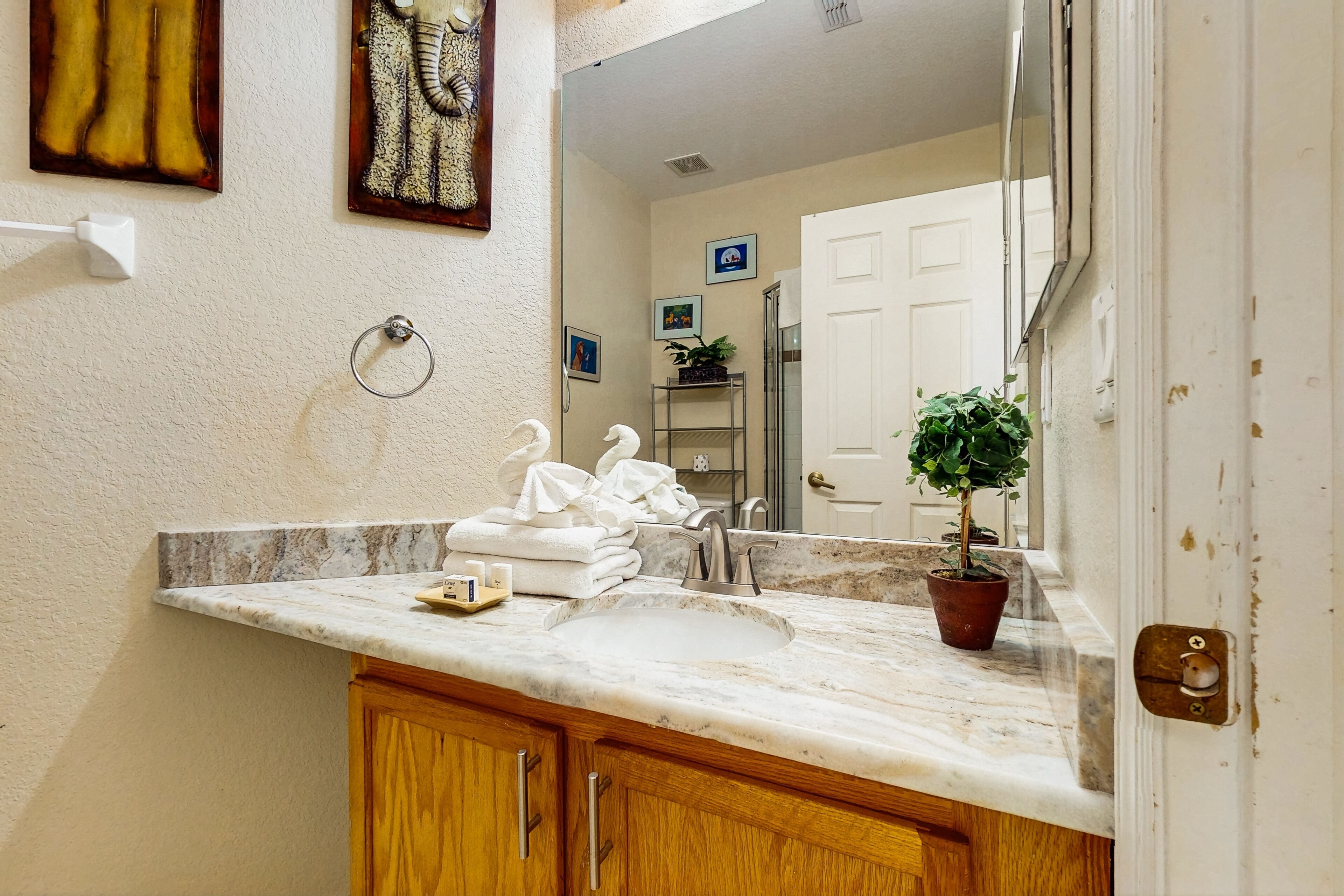 Une salle de bain avec un lavabo en marbre, des meubles en bois, un porte-serviettes et une plante en pot.