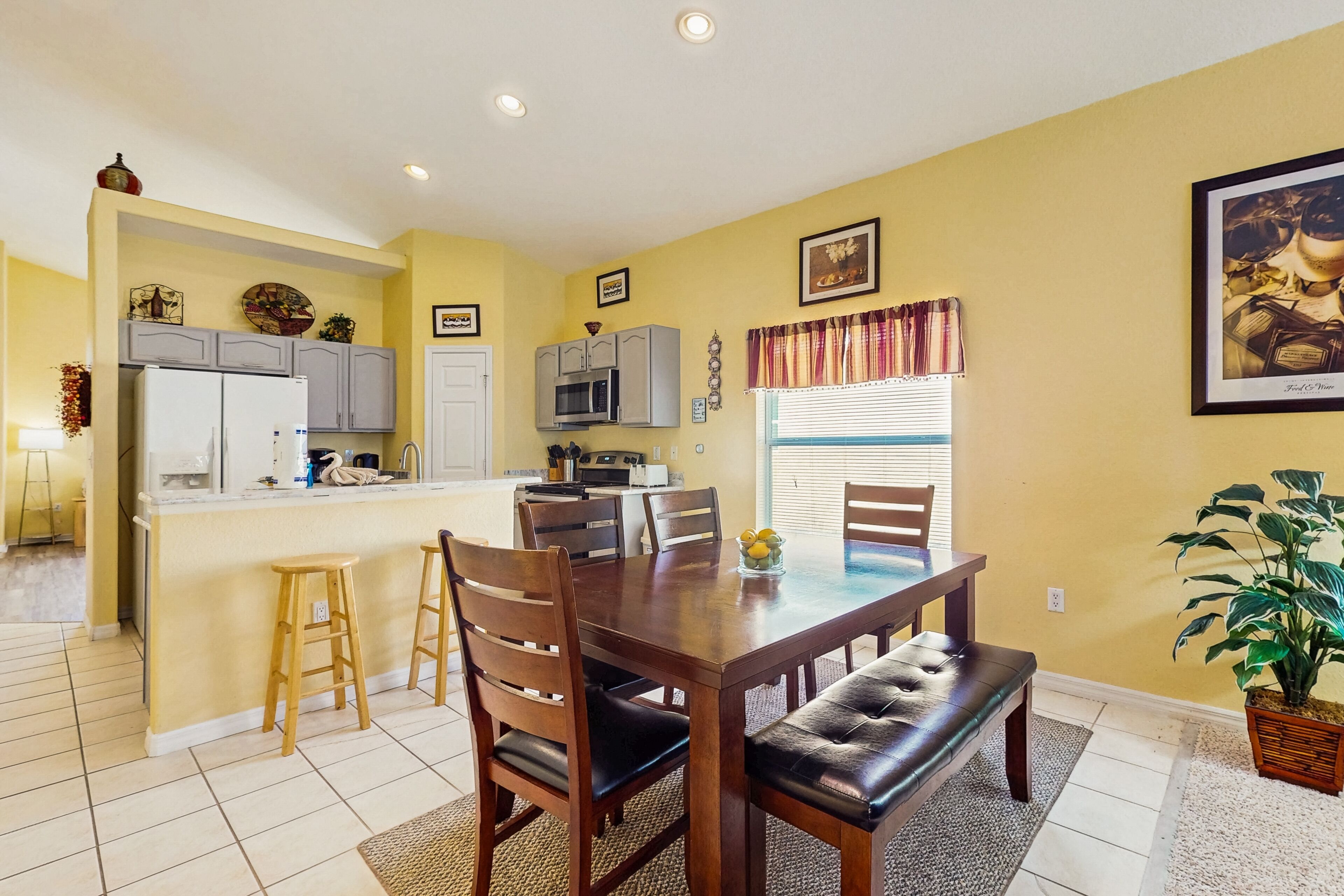A dining area with a wooden table and chairs, a kitchen with cabinets and appliances, and a potted plant.