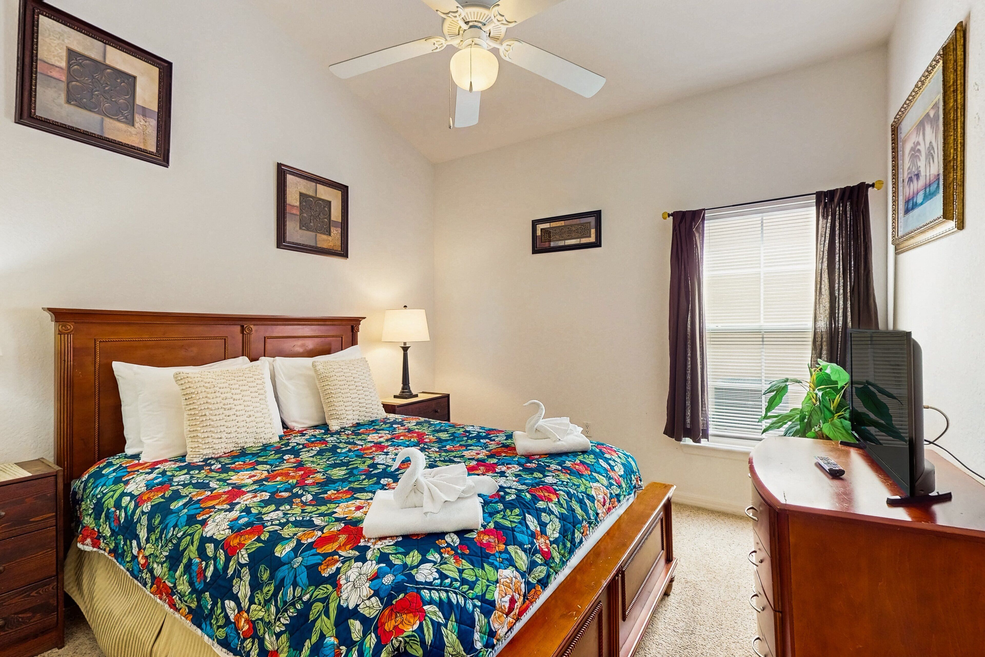 A bedroom with a bed, a nightstand, a desk, a television, and a ceiling fan.