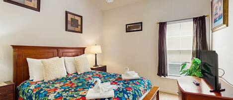 A bedroom with a bed, a nightstand, a desk, a television, and a ceiling fan.