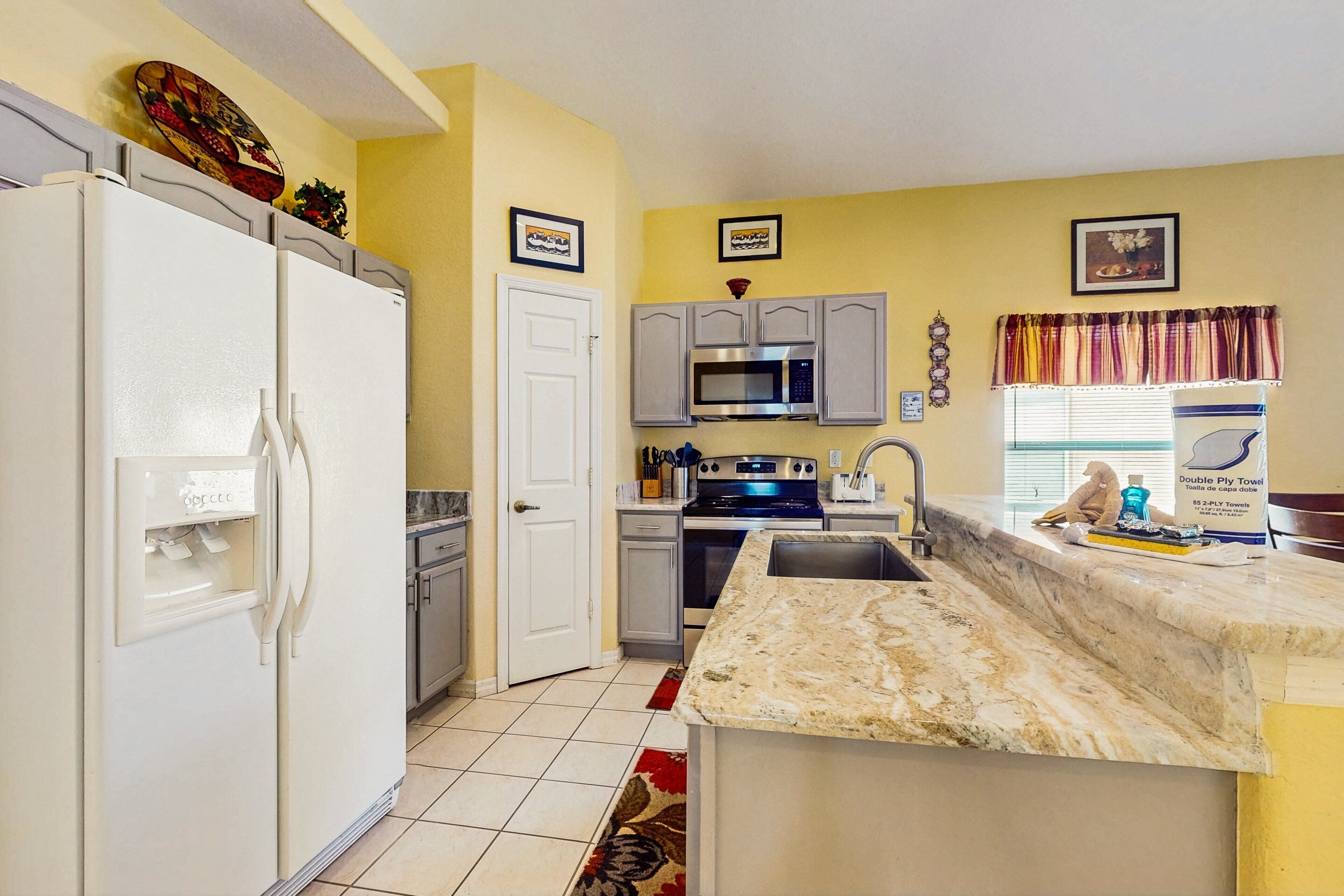 A kitchen with a refrigerator, microwave, oven, sink, and a marble countertop.