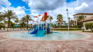 Un parc aquatique avec un toboggan bleu, des palmiers et un chemin pavé de briques.