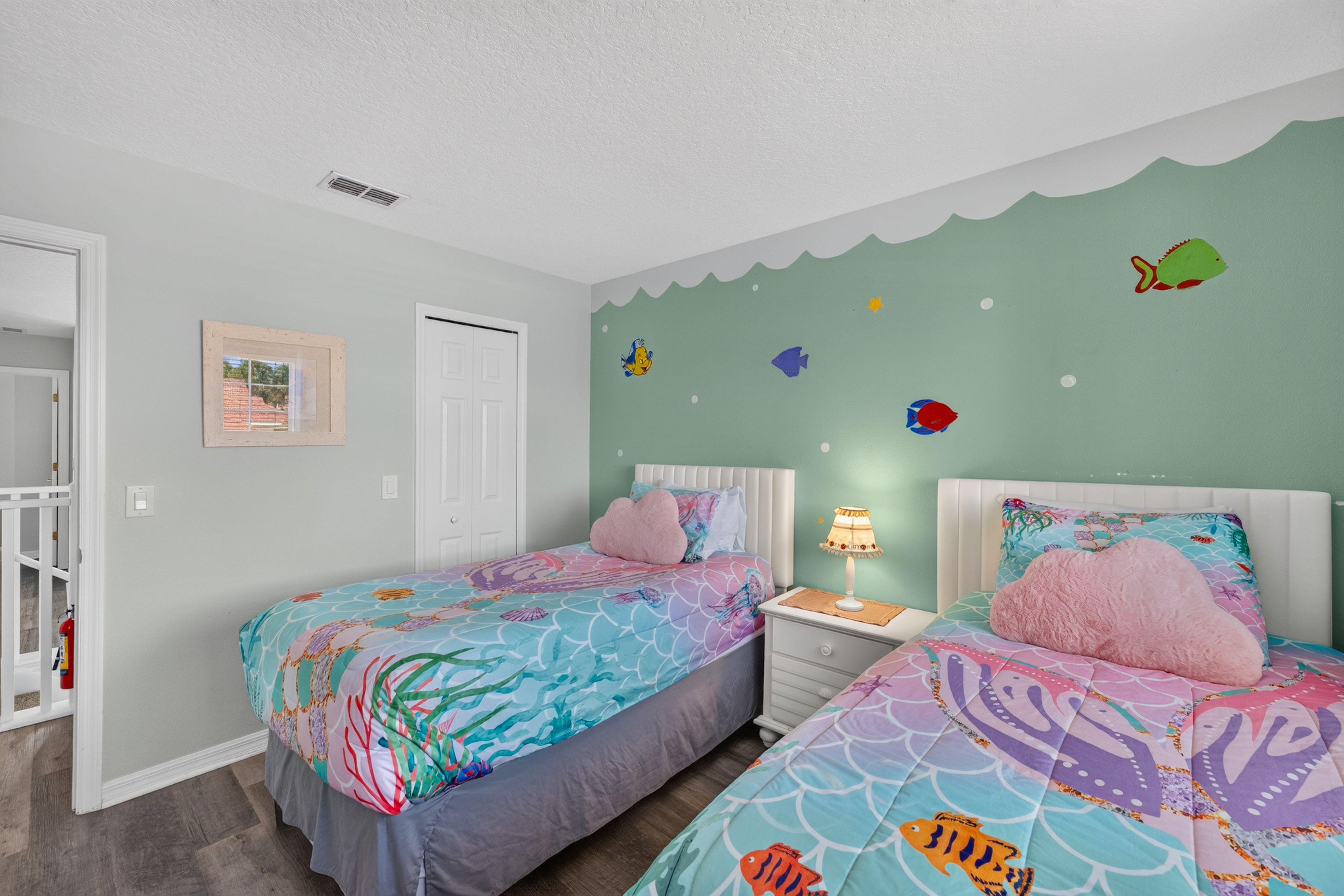 A bedroom with two beds, a nightstand with a lamp, a door, and a wall with fish decals.