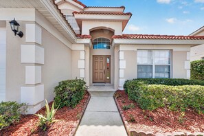A residential building with a central entrance, a covered porch, and a front yard with landscaping. - Wonderful Home For Theme Park Fun W/private Pool, Game Room, Wifi, AC, Patio, WD (Davenport)
