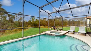 A swimming pool with a hot tub, surrounded by a glass enclosure, with chairs and a view of a grassy area and trees. - Wonderful Home For Theme Park Fun W/private Pool, Game Room, Wifi, AC, Patio, WD (Davenport)