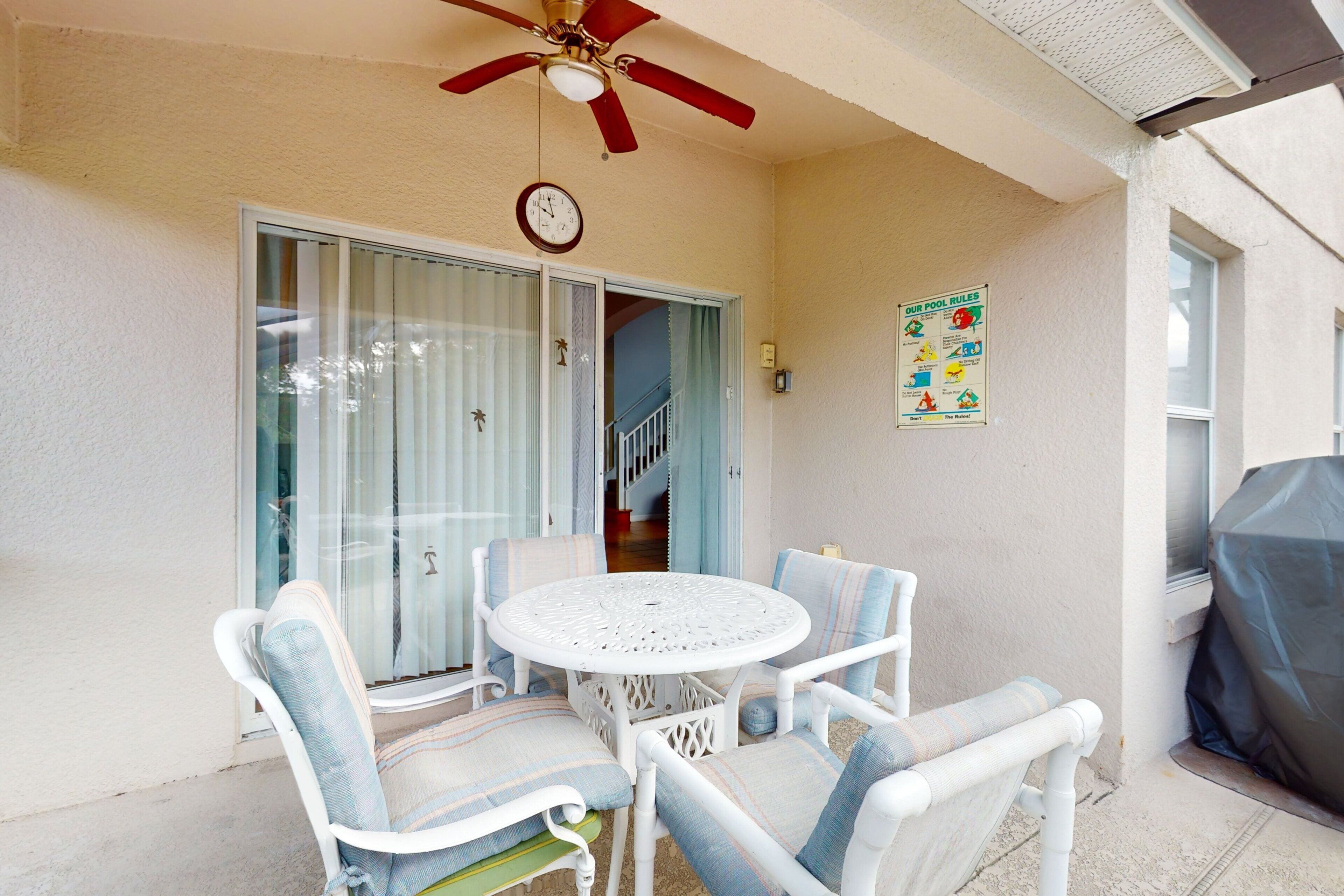 A patio with a round table and chairs, a ceiling fan, a clock, and a pool rules sign.