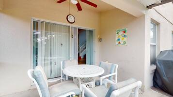 A patio with a round table and chairs, a ceiling fan, a clock, and a pool rules sign.