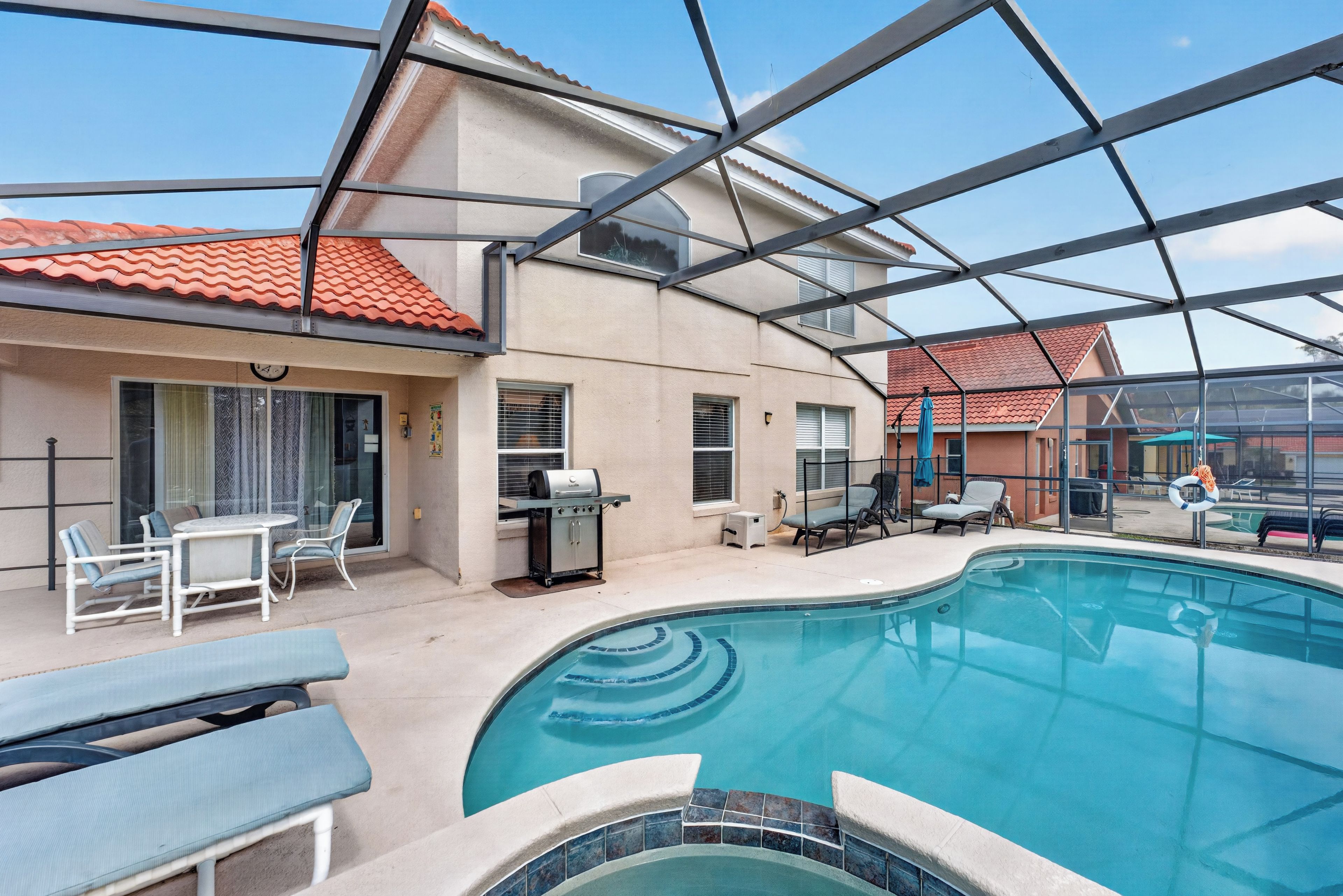 An indoor swimming pool with a clear view of the surrounding area, including a barbecue setup and lounge chairs.