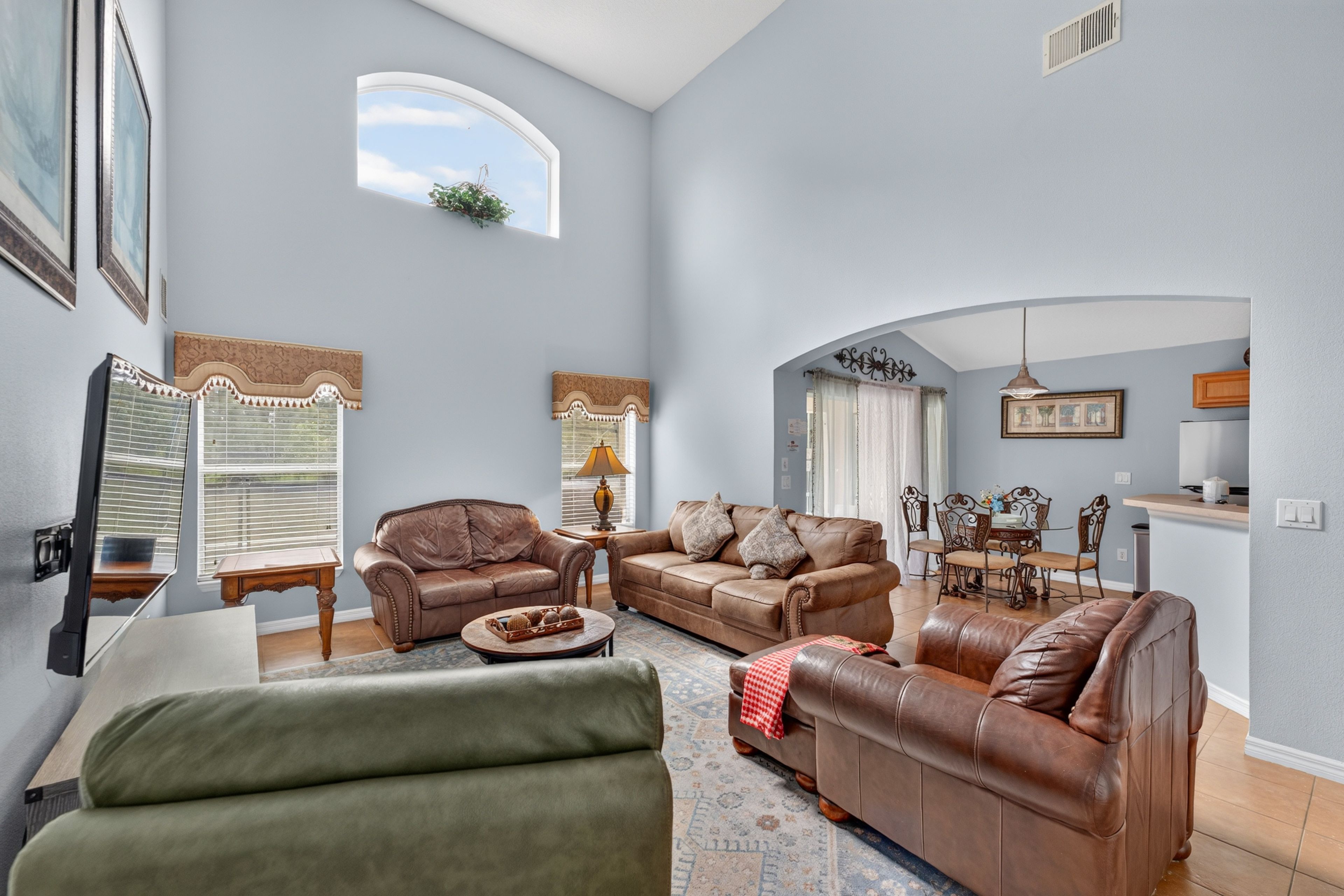 A spacious living room with a high ceiling, a dining area with a chandelier, and a kitchen with a modern design.