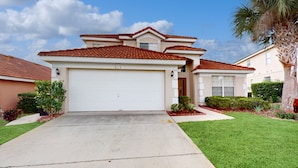 A two-story house with a red-tiled roof, a white garage door, and a well-maintained lawn. - Wonderful Home For Theme Park Fun W/private Pool, Game Room, Wifi, AC, Patio, WD (Davenport)