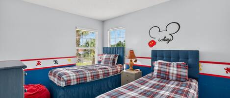 A bedroom with two beds, a red bean bag, and a wall decoration.
