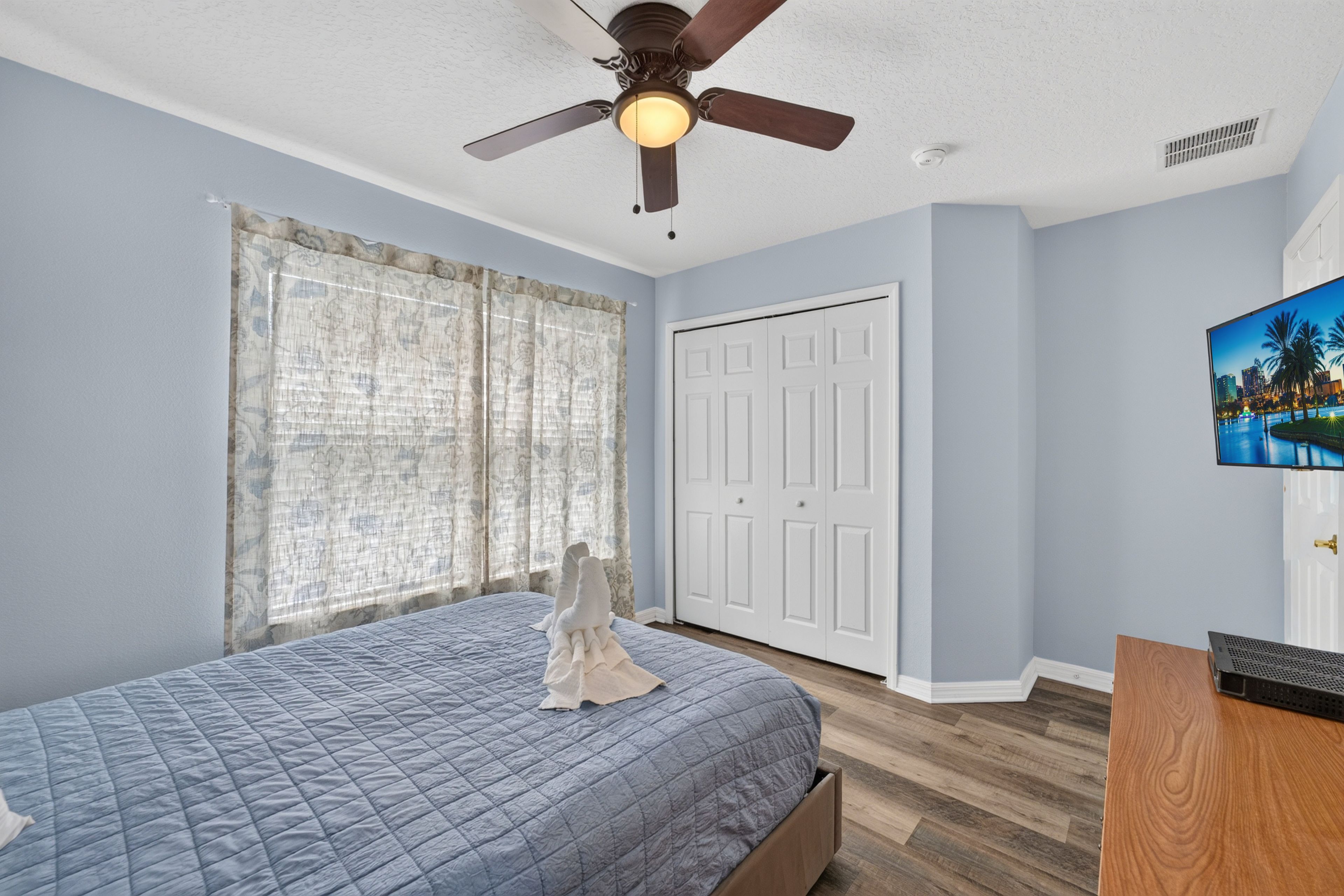 A bedroom with a bed, a ceiling fan, a door, and a painting on the wall.