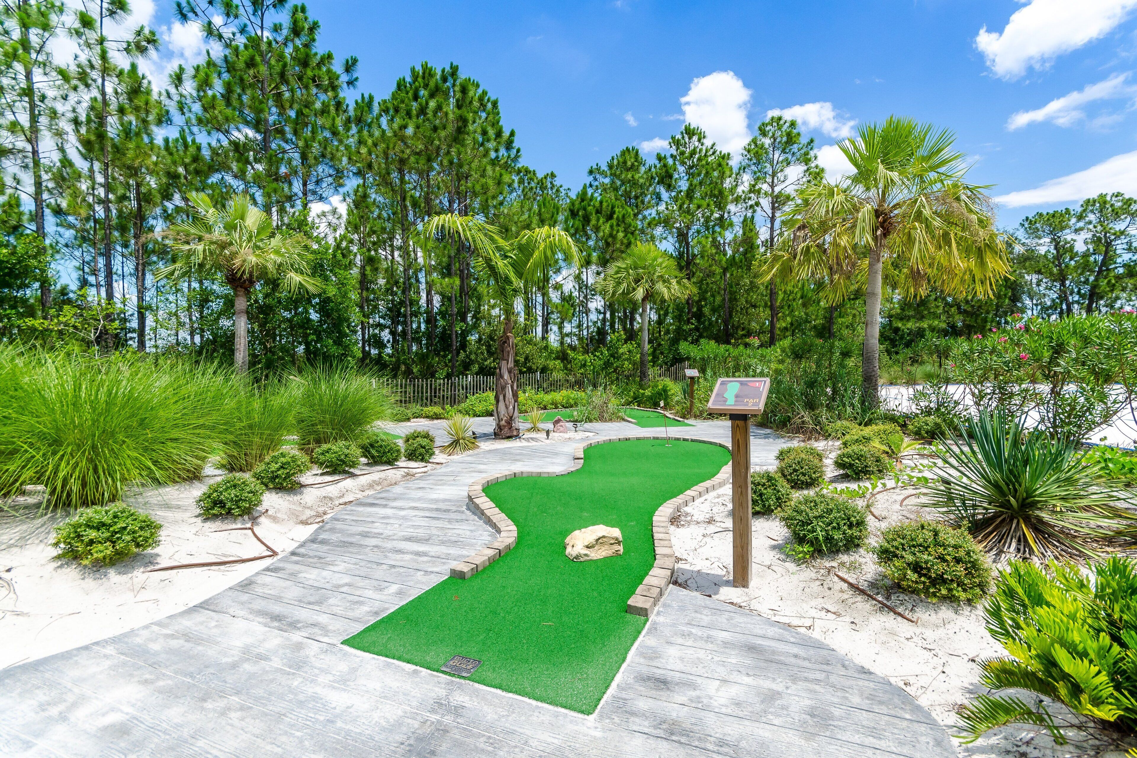 Un parcours de golf doté d’un sentier en bois, d’une pelouse artificielle verte et d’une végétation luxuriante tout autour.