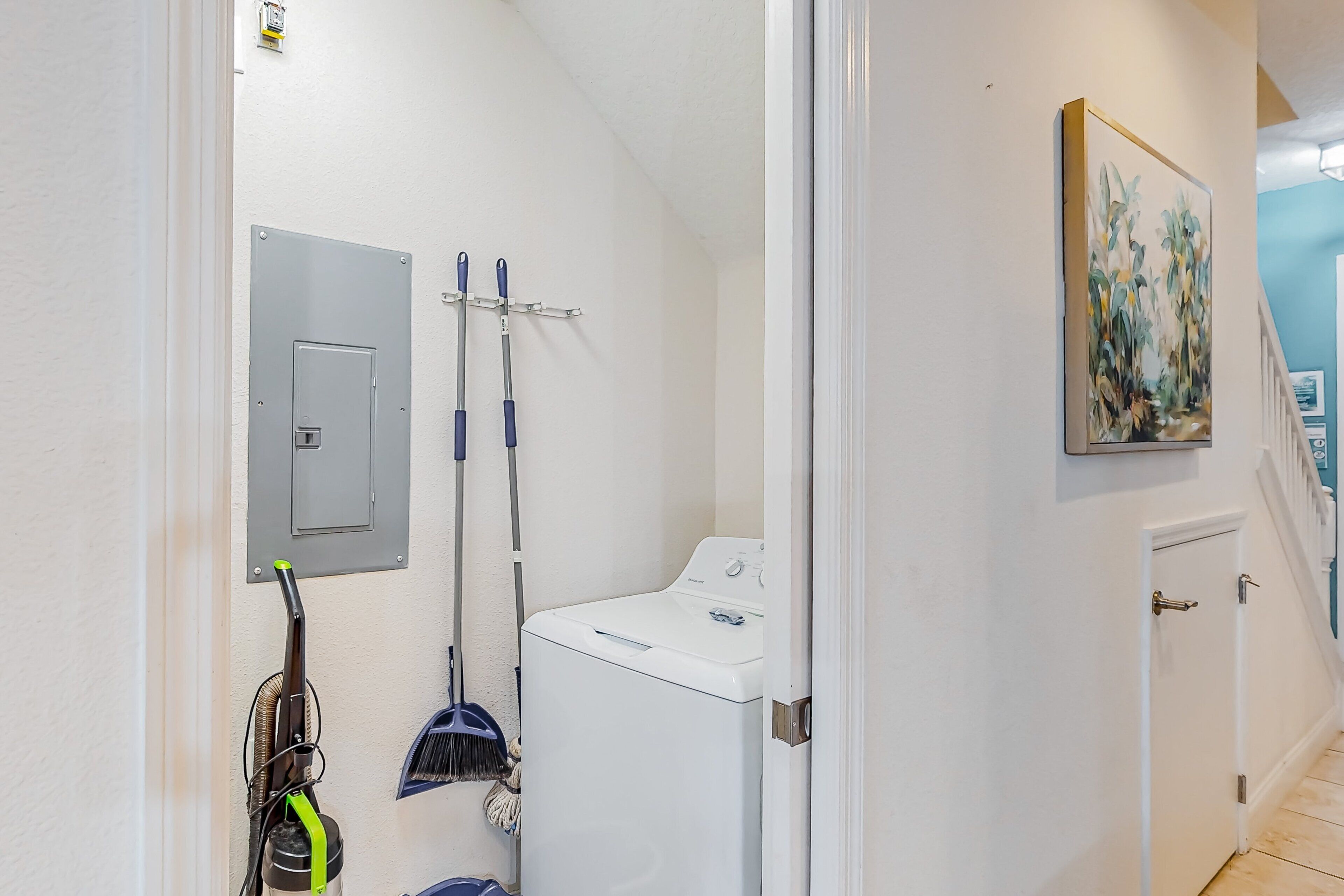 A laundry area with a washing machine, a broom, a vacuum cleaner, and a mop.