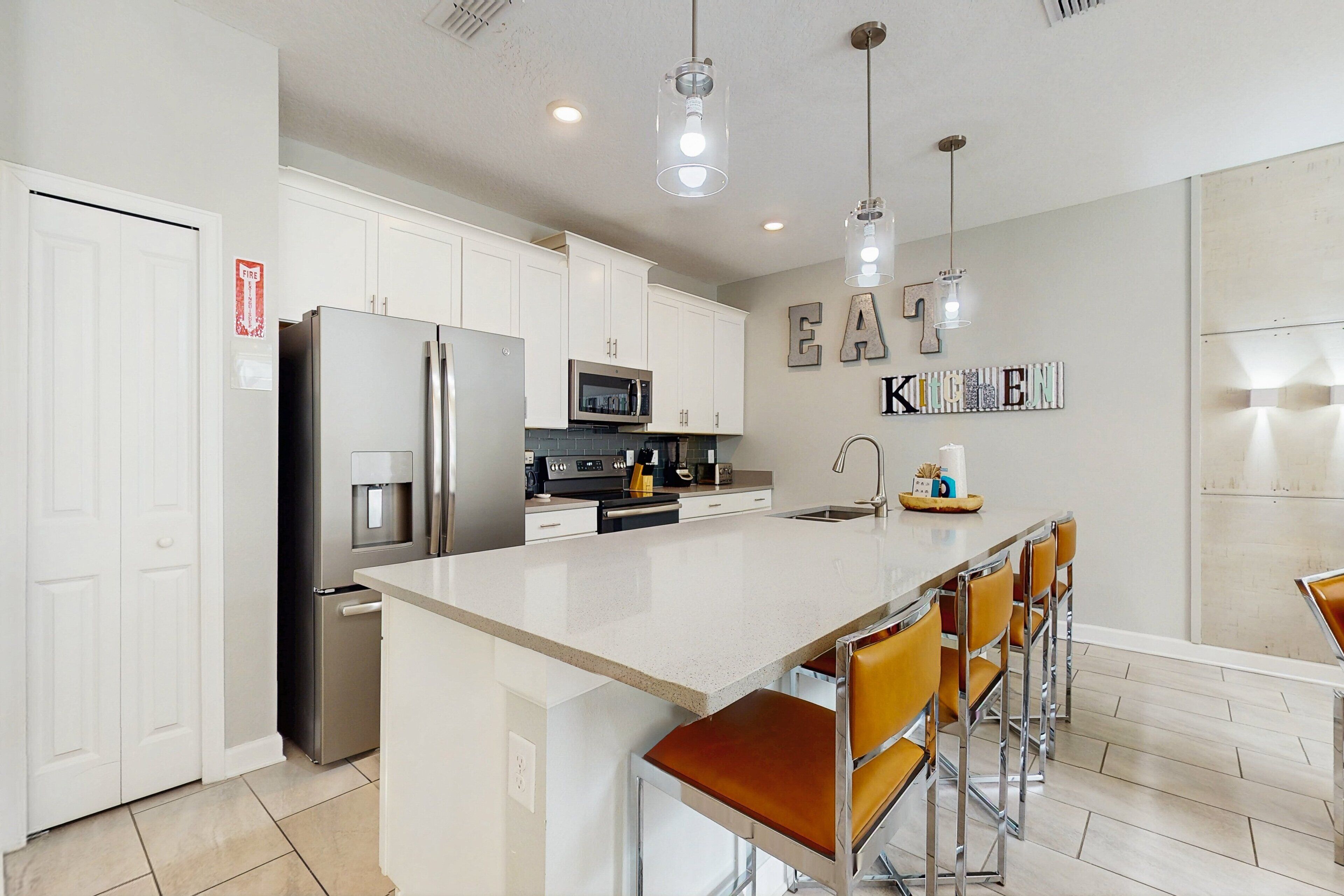 A modern kitchen with white cabinets, stainless steel appliances, a central island with bar stools, and pendant lighting.
