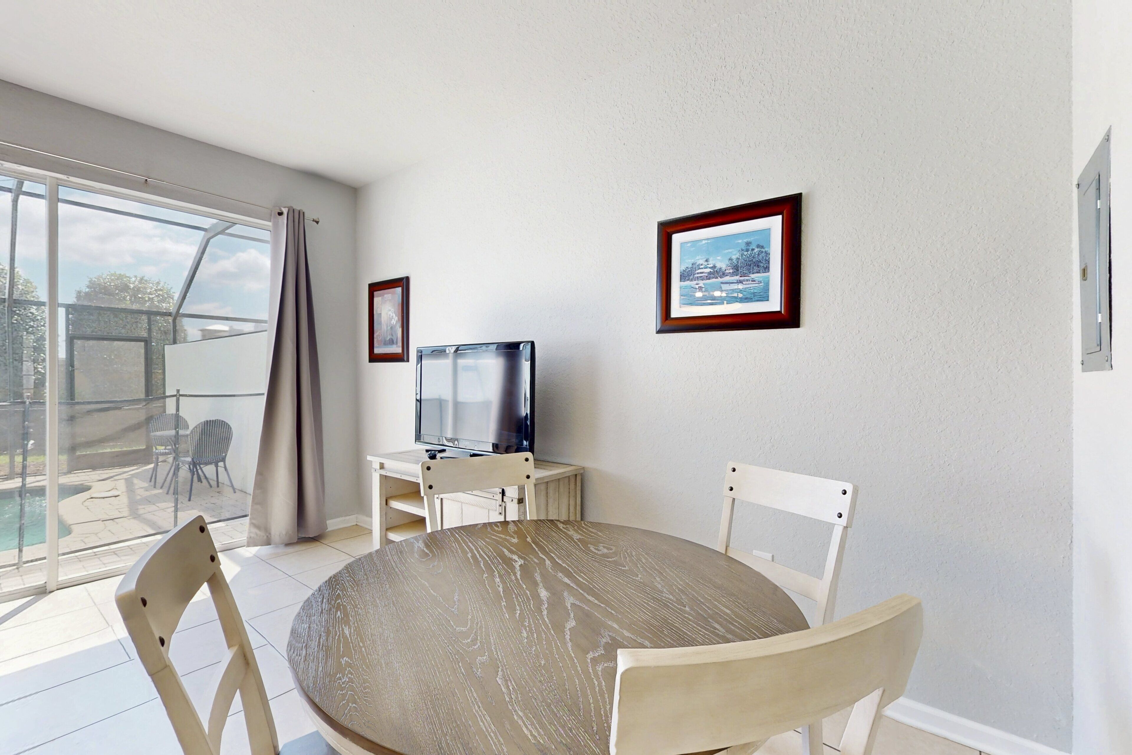 Un comedor con una mesa redonda, cuatro sillas, un televisor sobre un mueble bajo y cuadros enmarcados en la pared.