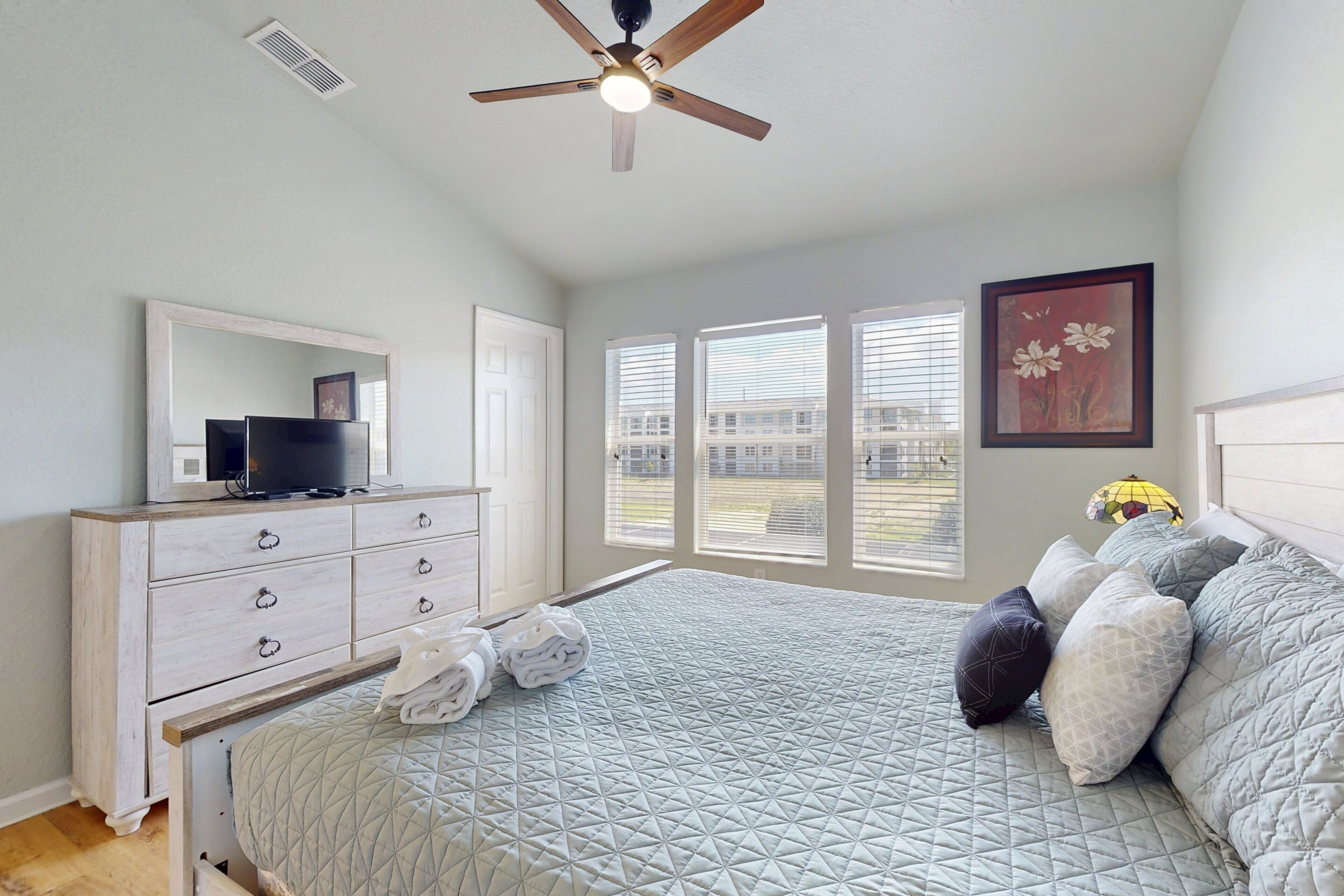 A bedroom with a bed, a dresser, a television, and a ceiling fan.