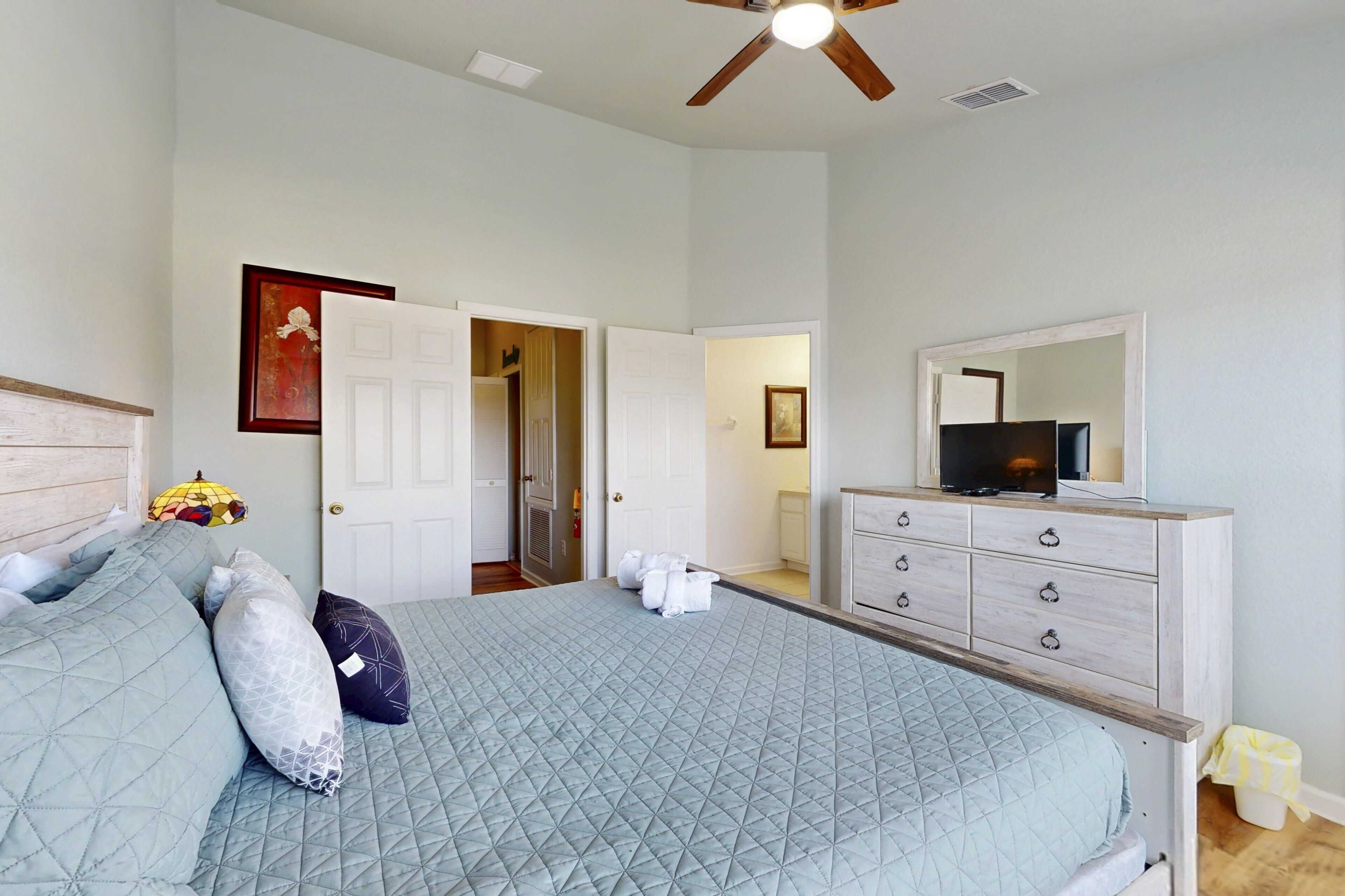 A bedroom with a bed, a dresser, a television, and a ceiling fan.