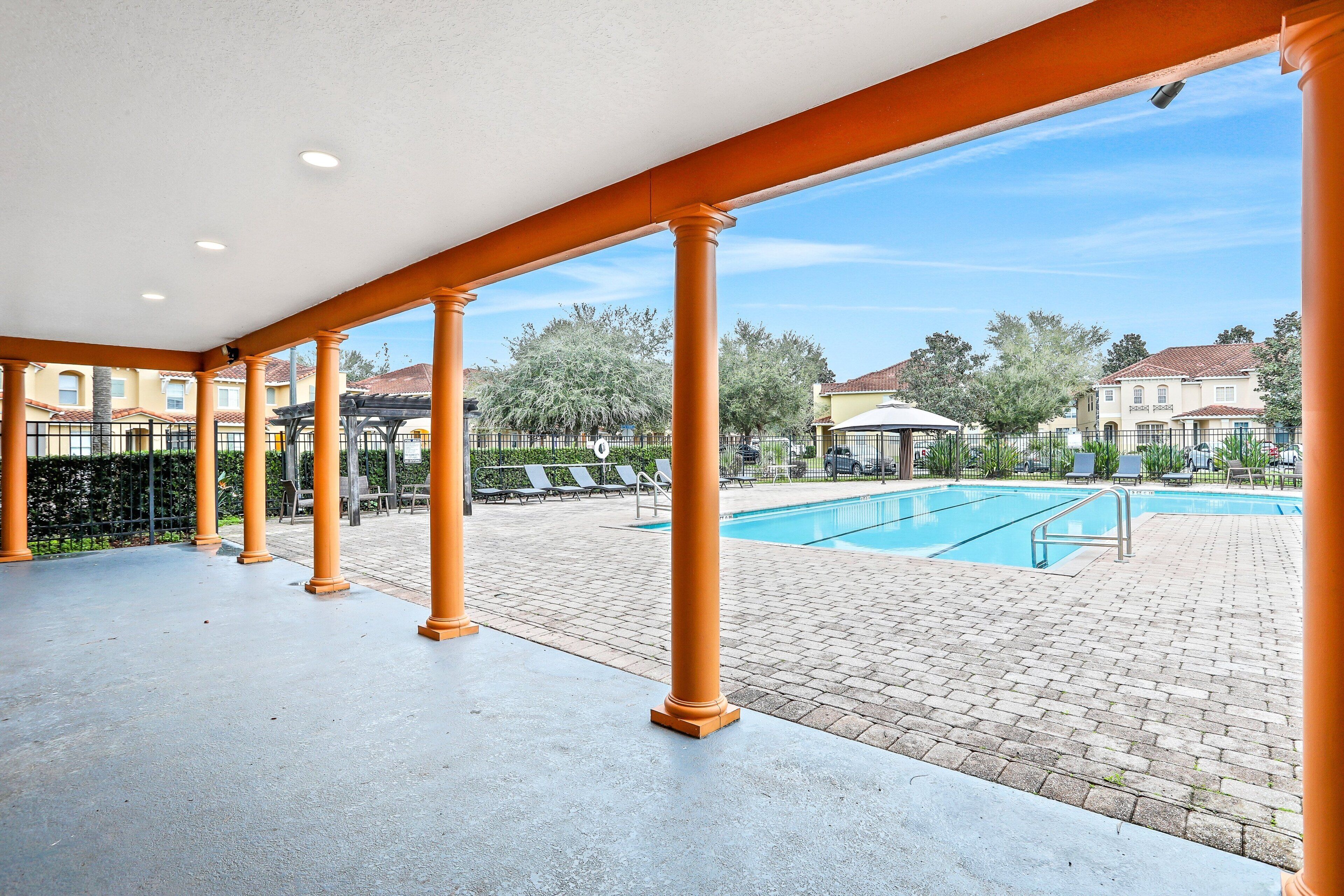 A covered outdoor area with columns, a pool, and a view of residential buildings.