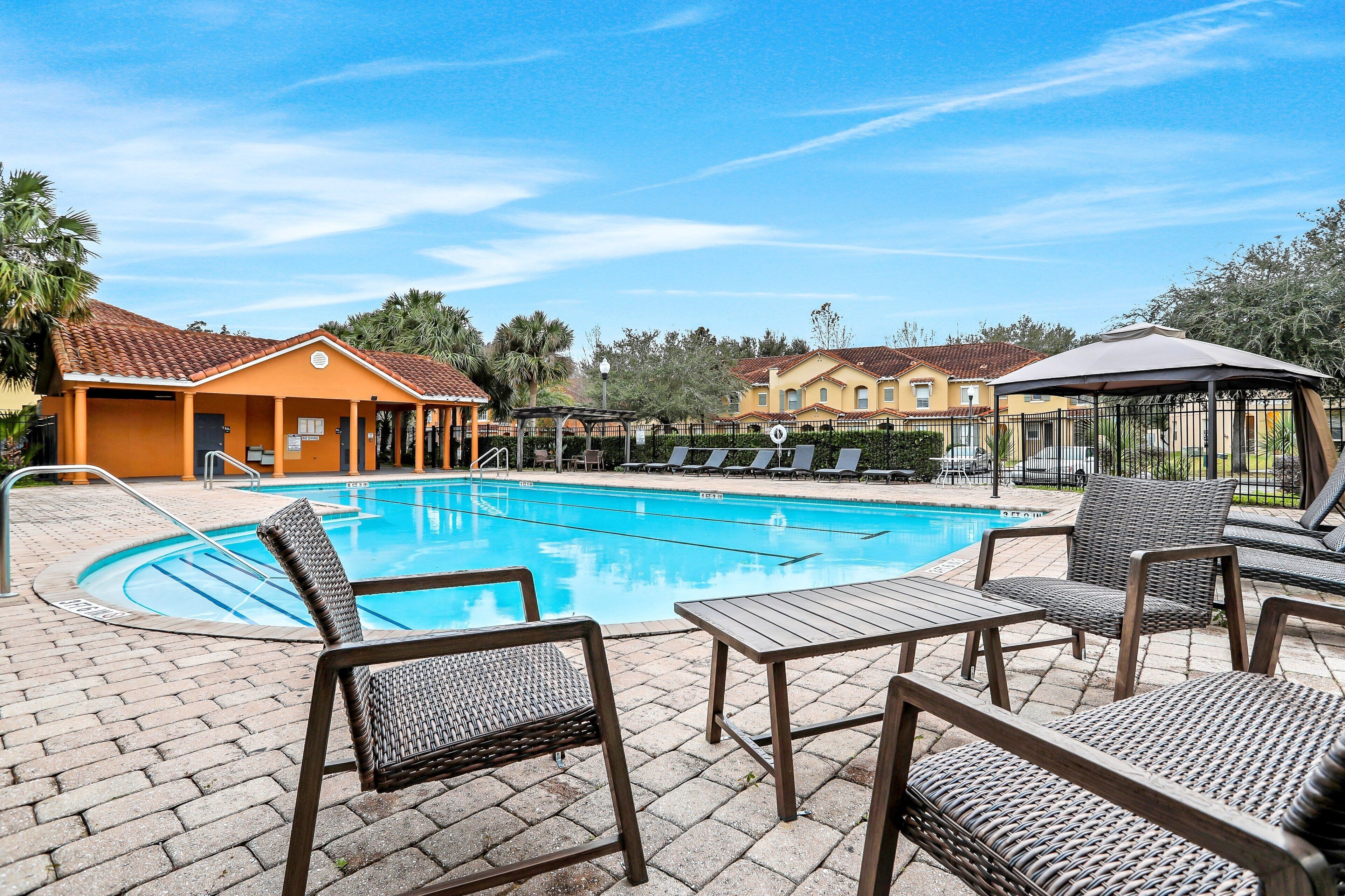 A swimming pool with lounge chairs and a gazebo, surrounded by a brick patio and buildings.