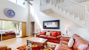 Ein geräumiges Wohnzimmer mit großem Fenster, einer Treppe, einem Ledersofa, einem Couchtisch und einem Teppich.