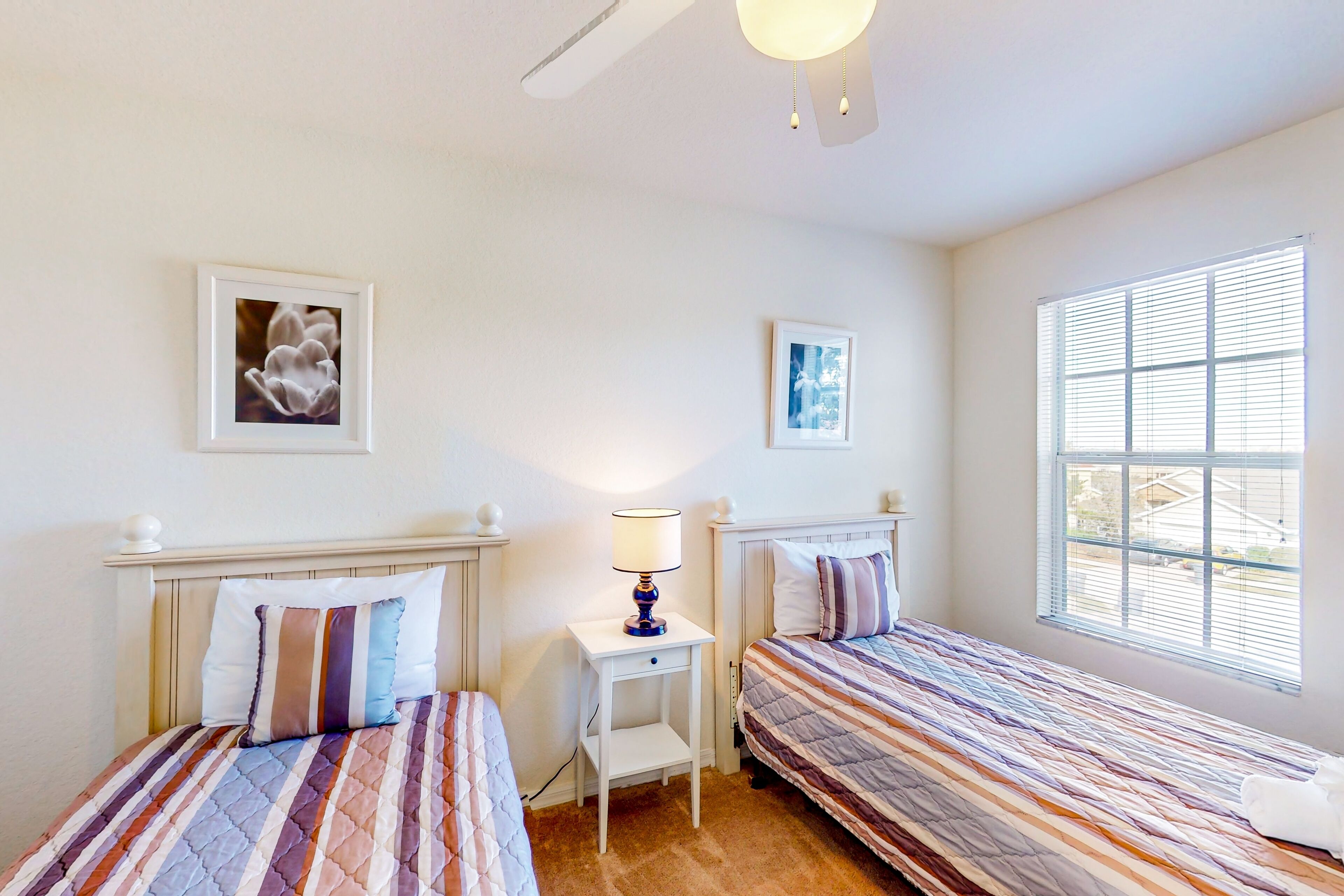 A bedroom with two beds, a nightstand with a lamp, and a window with blinds.