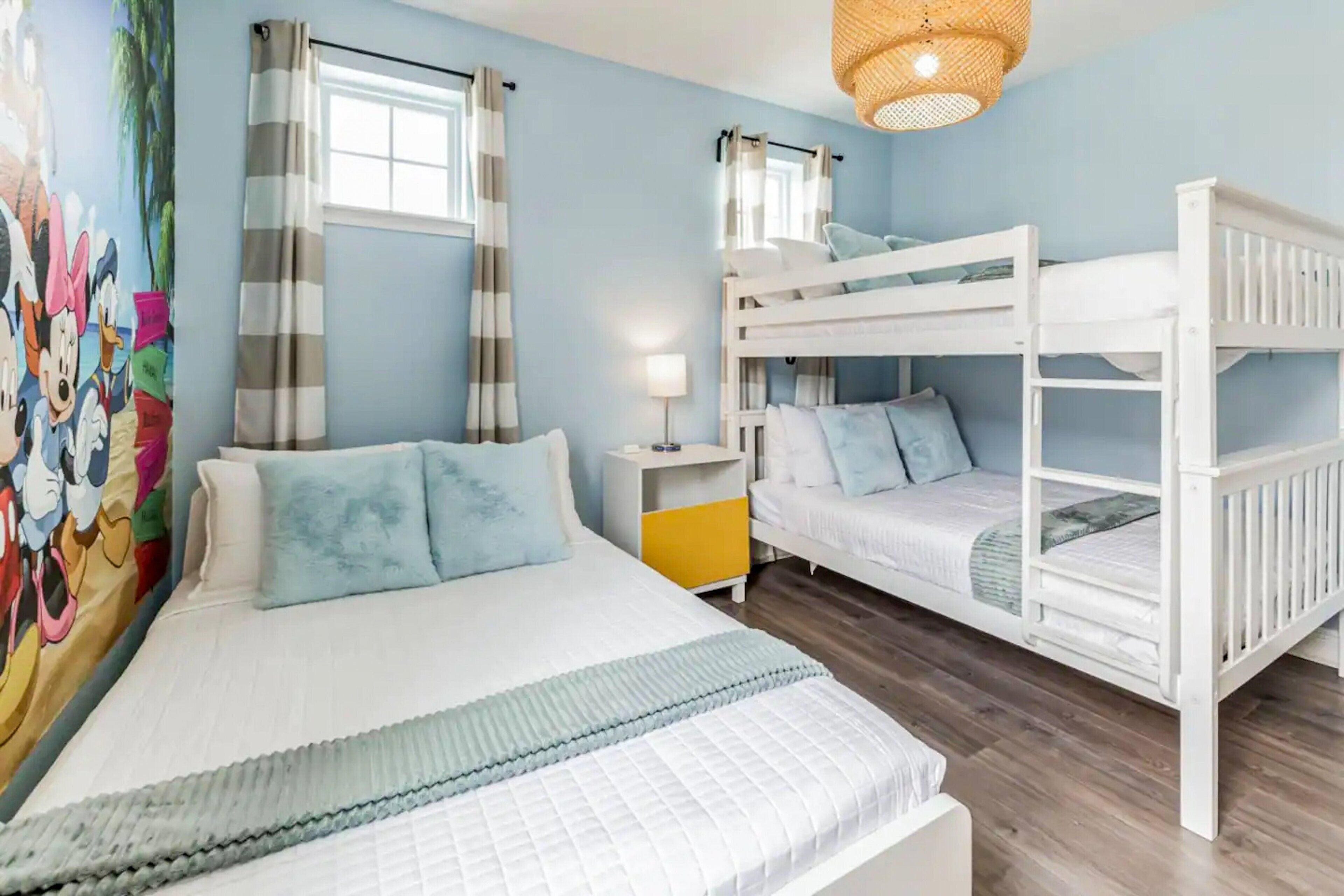 Une chambre avec un lit superposé, un lit simple, une table de chevet, une lampe et une fresque murale.