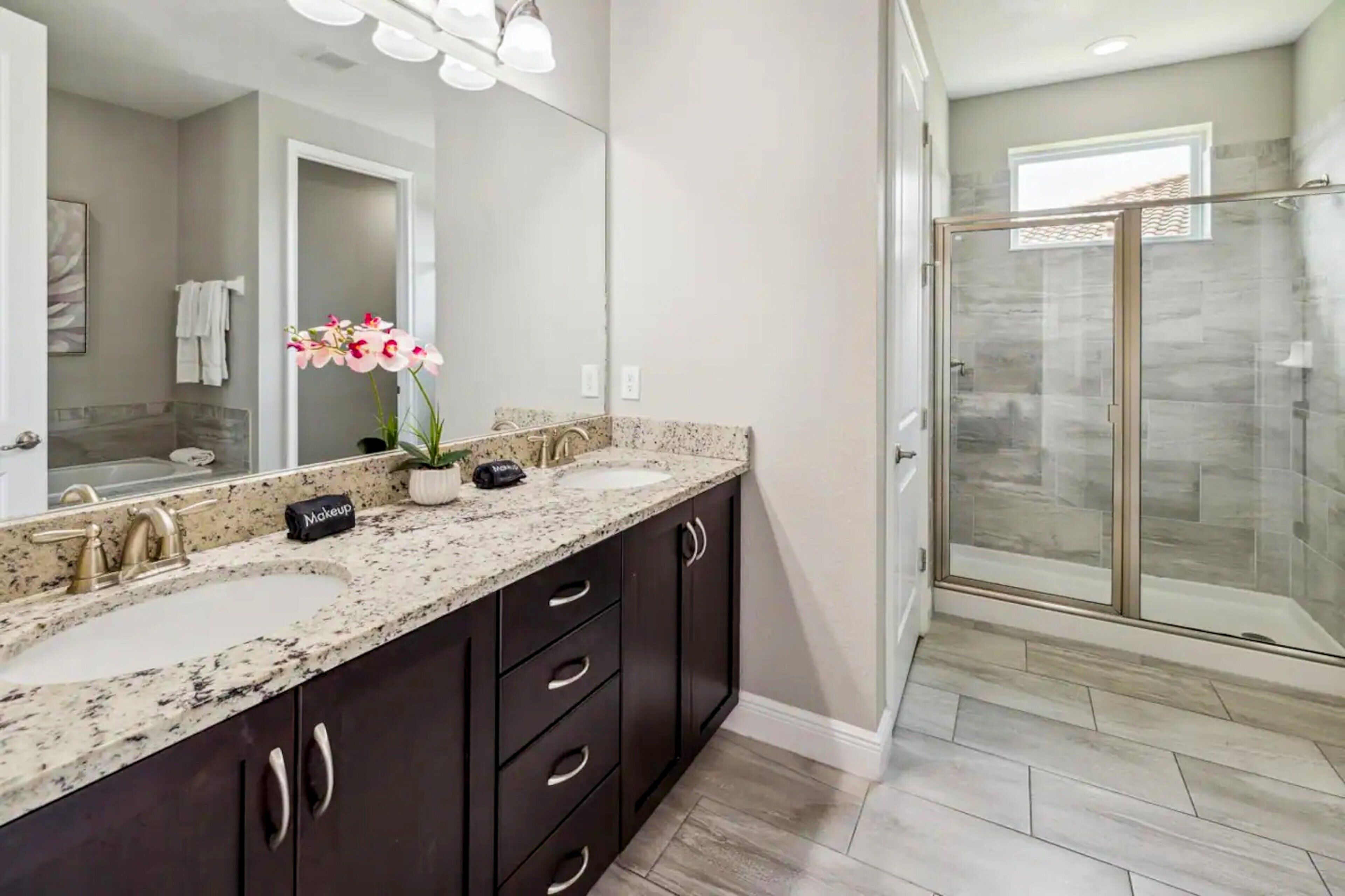 A bathroom with two sinks, dark cabinets, a large mirror, and a glass shower enclosure.