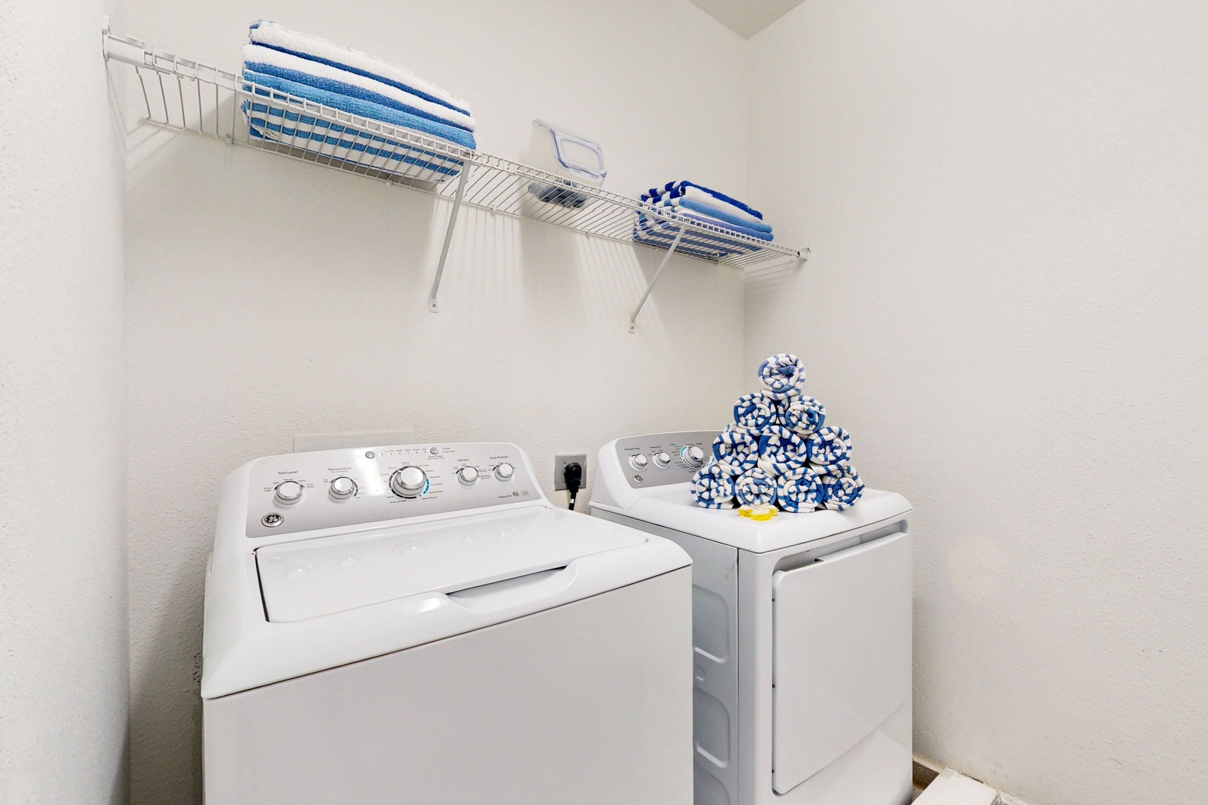 A laundry area with two white washing machines, a metal drying rack with folded towels, and a wall-mounted towel rack.