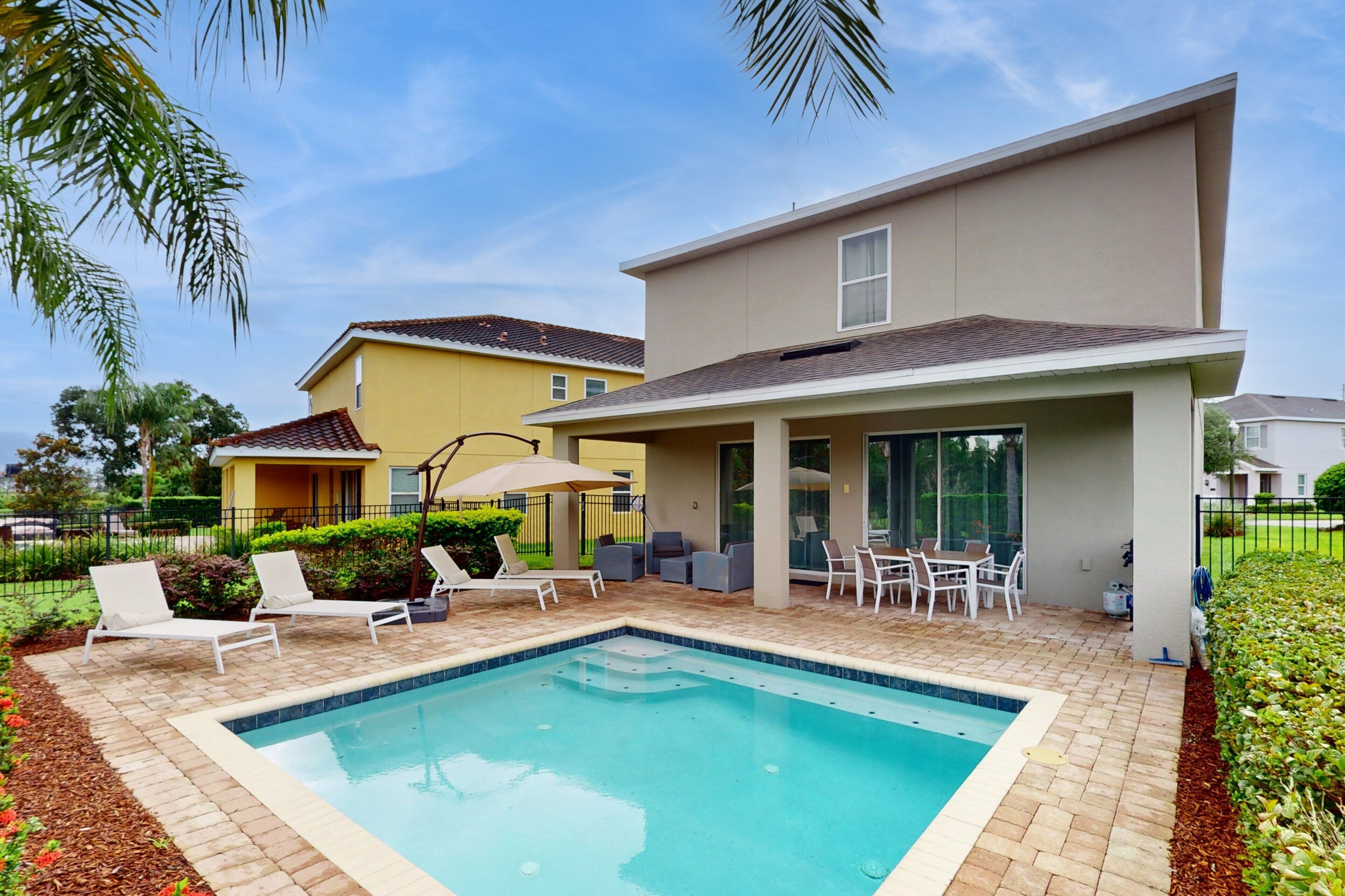 A swimming pool with lounge chairs, a covered patio, and a two-story building with a flat roof.