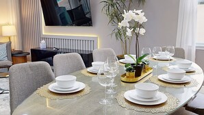 A dining area with a round table set for six, a television mounted on the wall, and a potted orchid plant. - Near Theme Parks, fun Filled Home With Harry Potter Bedroom, & Private Pool (Kissimmee)