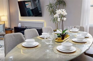 A dining area with a round table set for six, a television mounted on the wall, and a potted orchid plant. - Near Theme Parks, fun Filled Home With Harry Potter Bedroom, & Private Pool (Kissimmee)