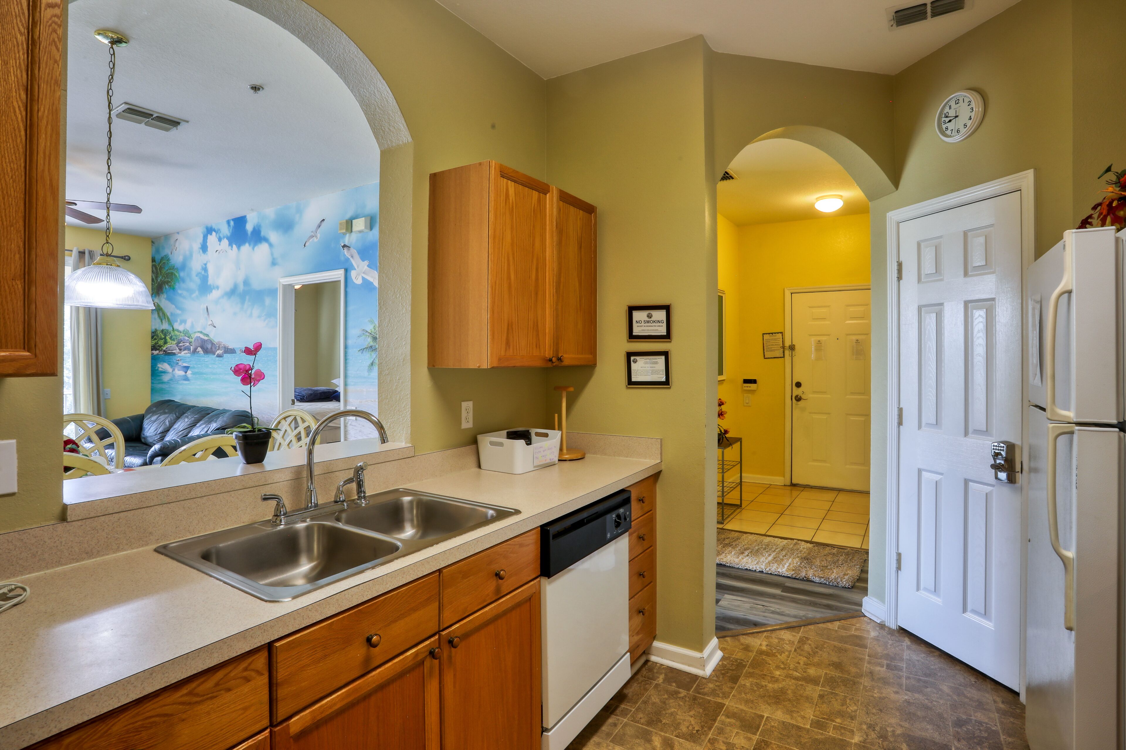 A kitchen with a double sink, wooden cabinets, a dishwasher, and a large mirror.