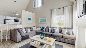 A modern living room with a sectional sofa, a dining area with a white table, and a kitchen in the background. - Spacious Condo With Themed Rooms, Foosball Table and Shared Pool (Kissimmee)