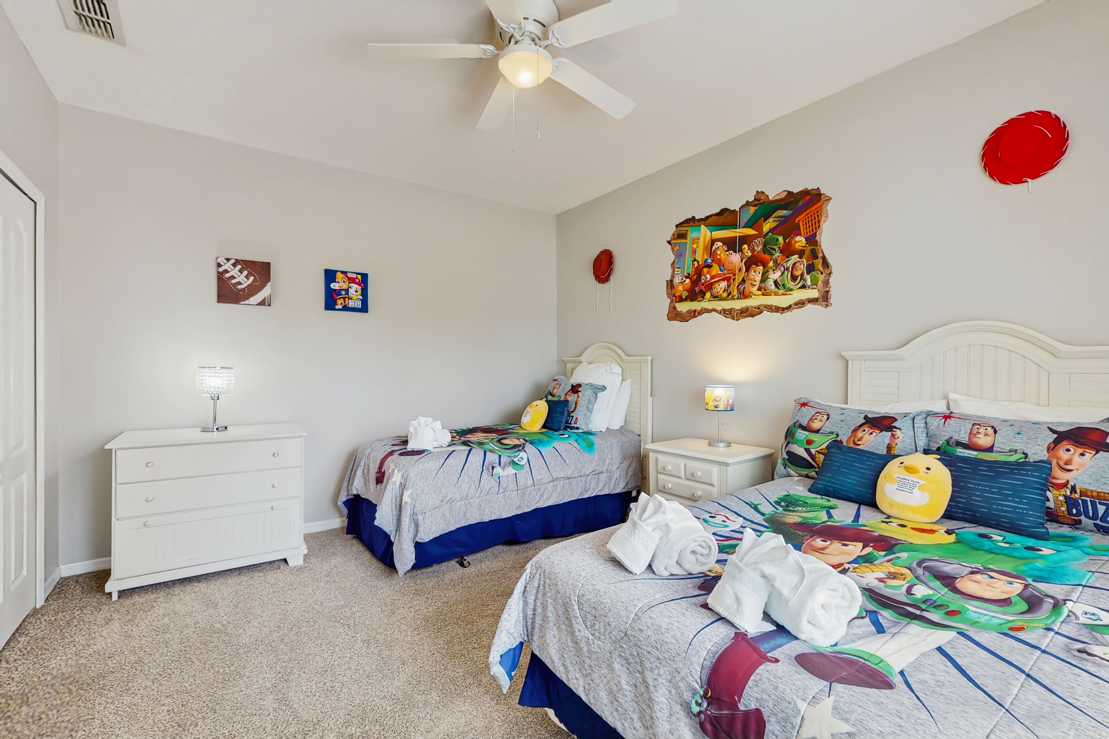 A bedroom with two beds, a ceiling fan, and a wall with artwork.