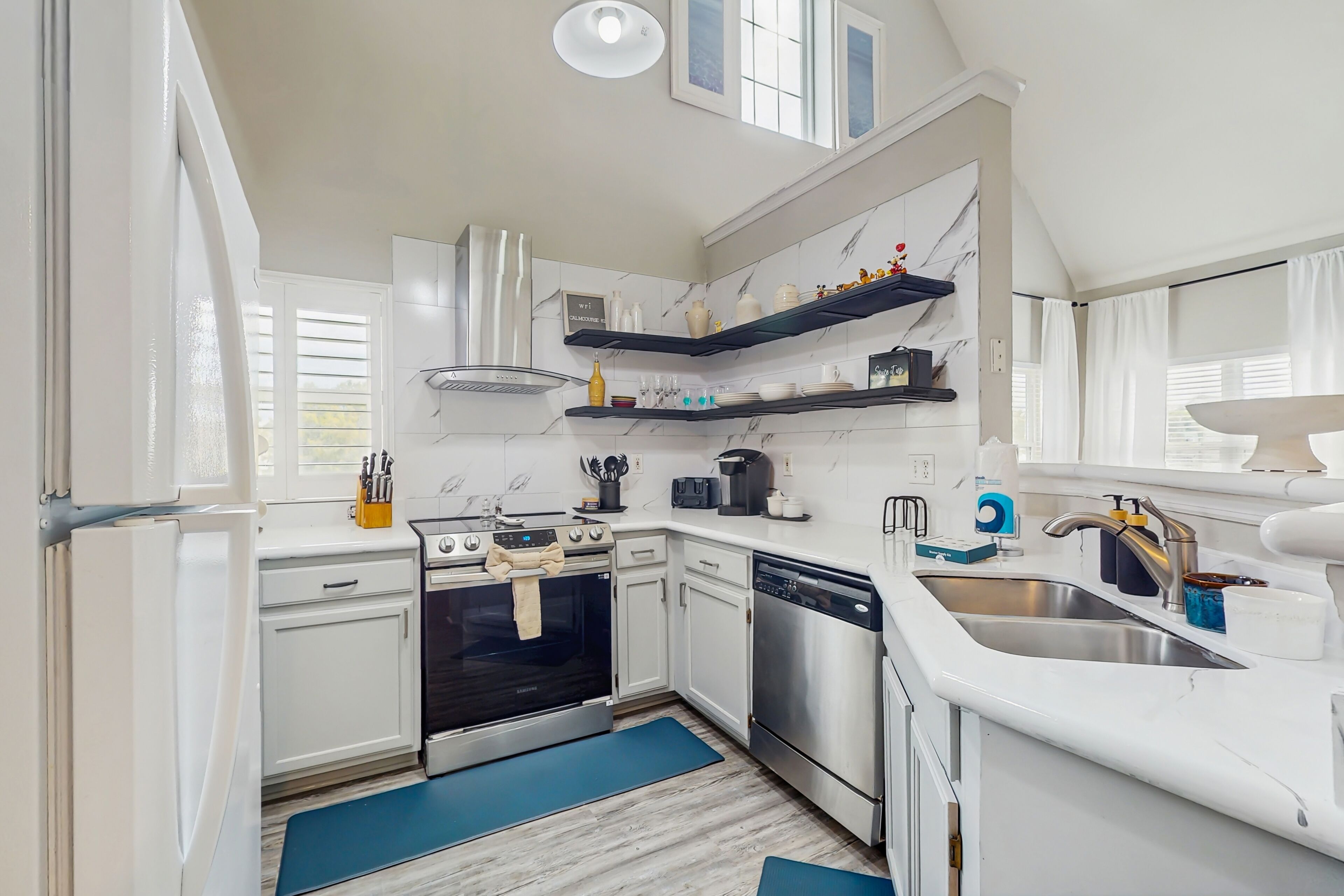 A modern kitchen with white cabinets, stainless steel appliances, and blue mats on the floor.
