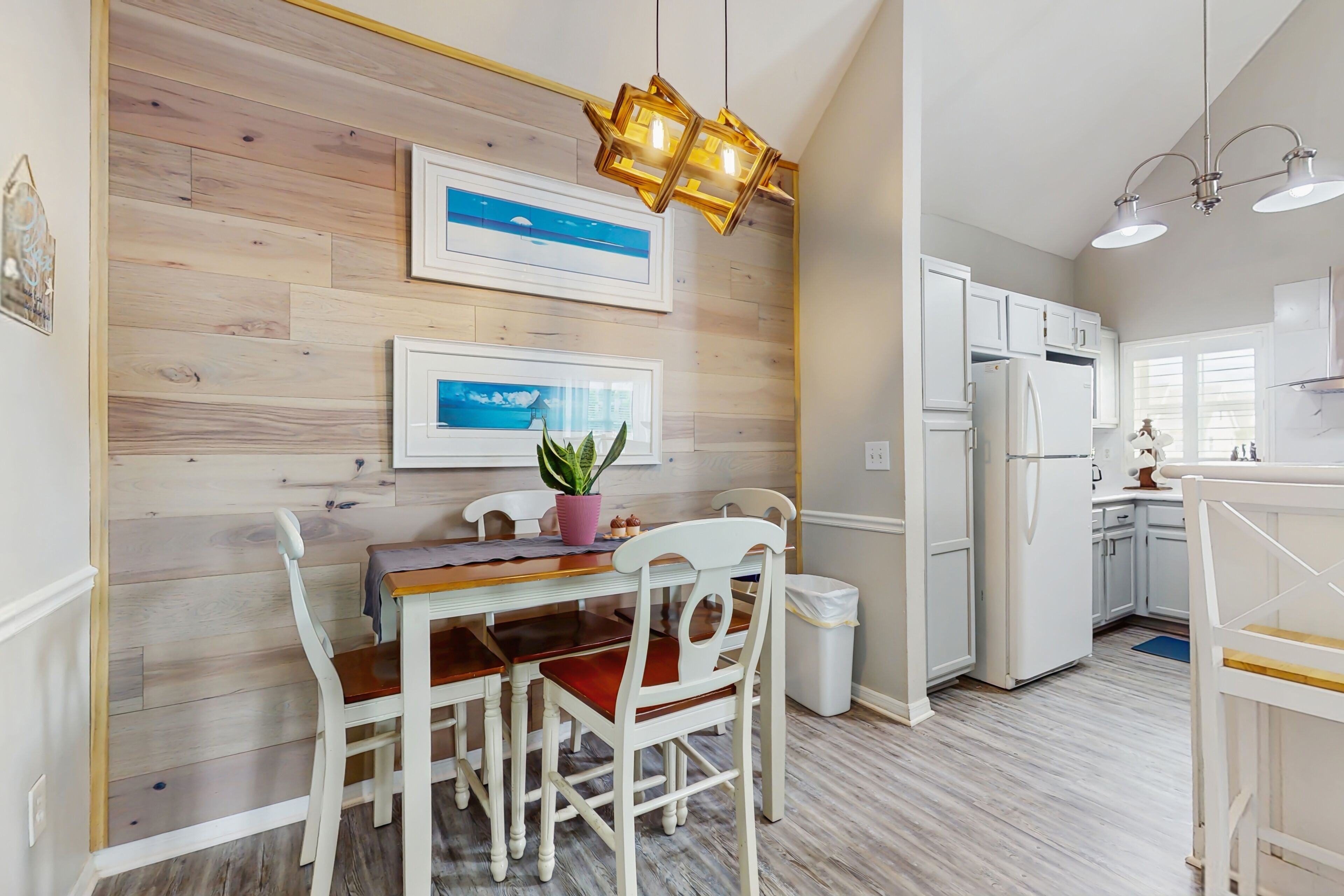 A modern kitchen with white cabinets, a wooden wall, and a dining area with a table and chairs.