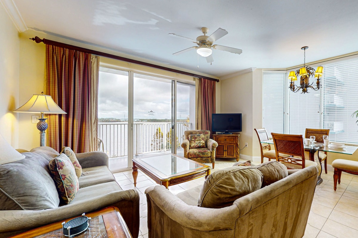 A spacious living room with a sofa, armchairs, a glass coffee table, a television, and a dining area with a chandelier.